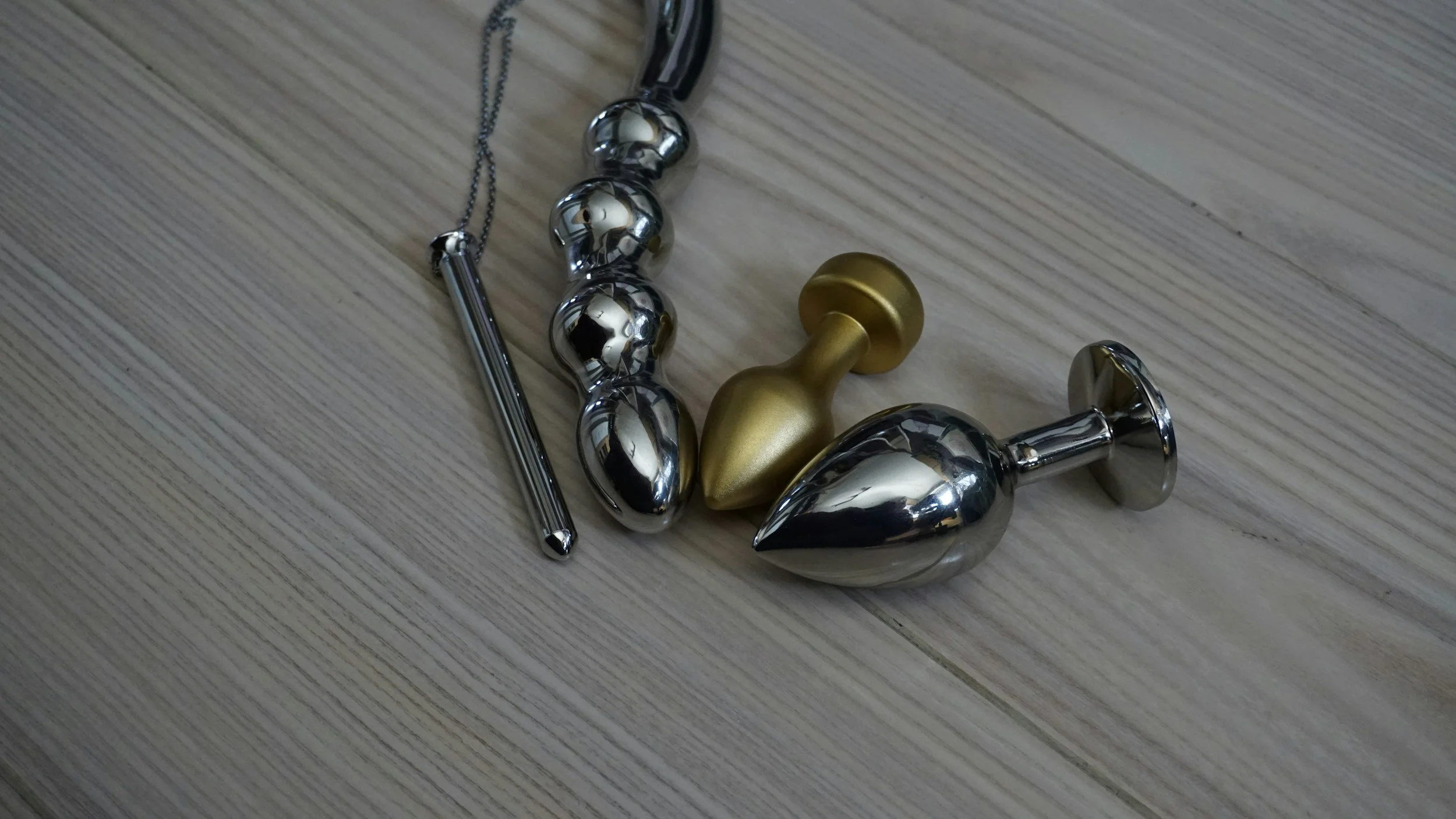 Assorted metallic sex toys on a wooden floor.