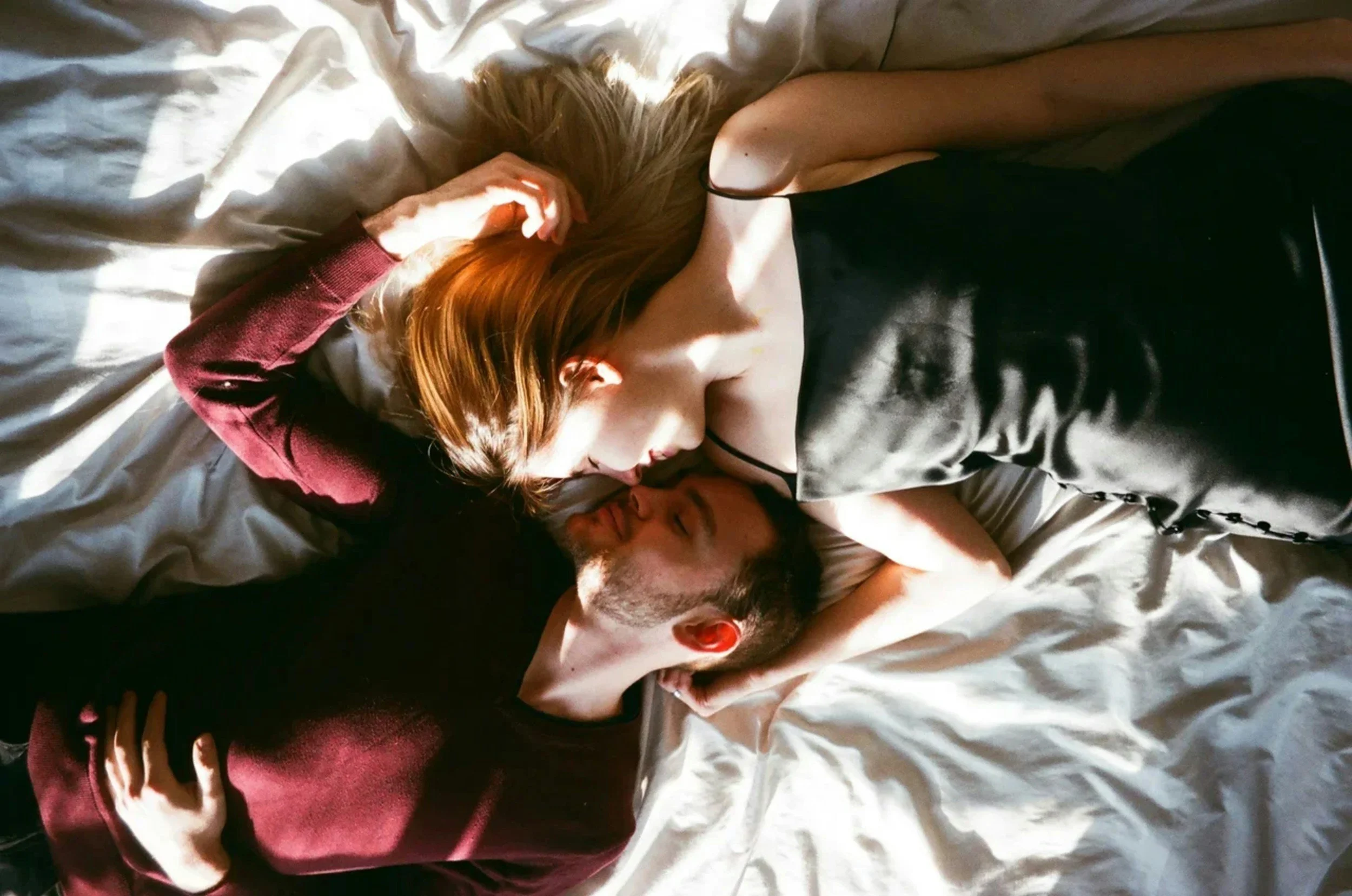 A couple lying on a bed, embracing and kissing, bathed in natural light.