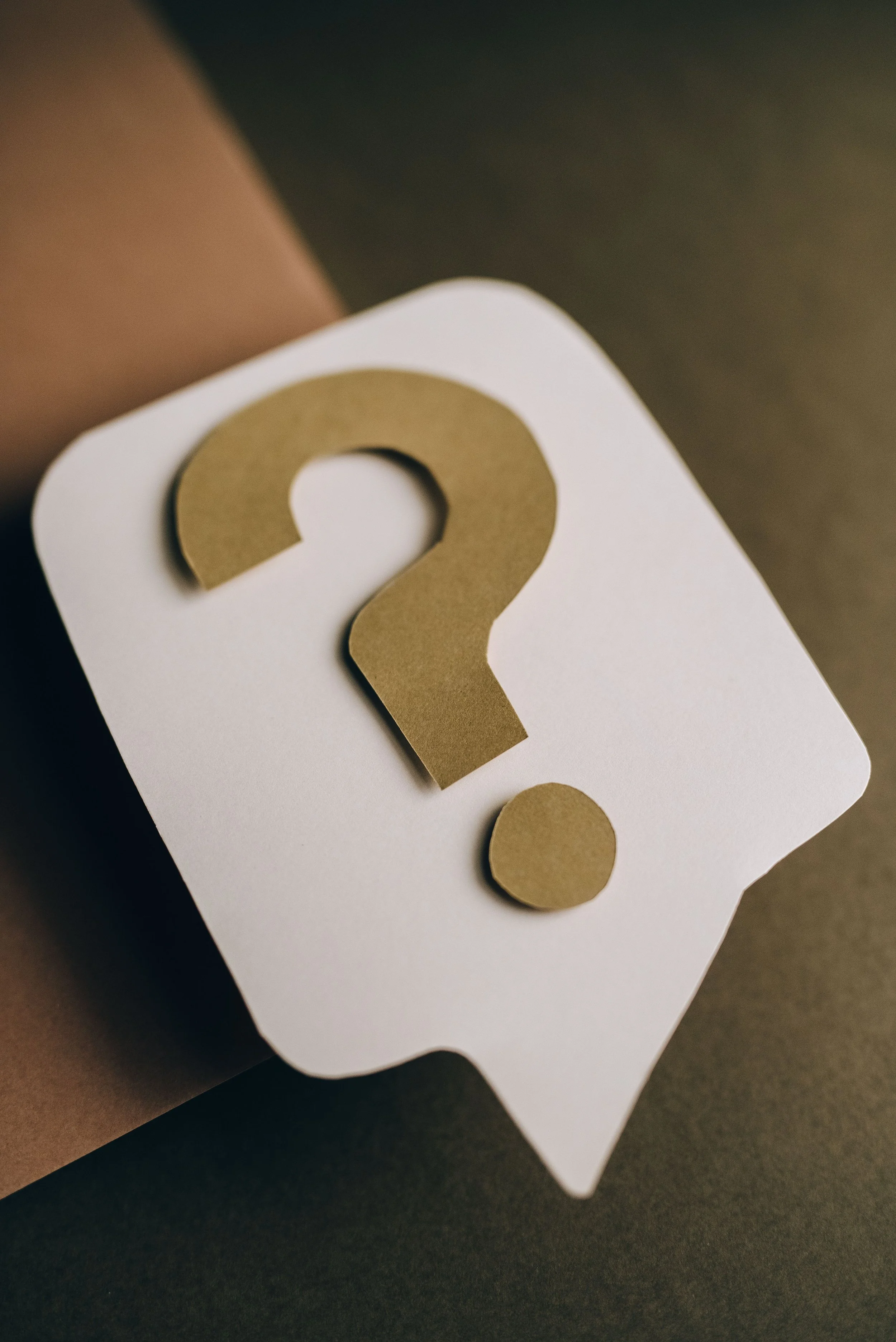 A brown paper roll with a white label and a large gold question mark sticker on top, resting on a dark surface.