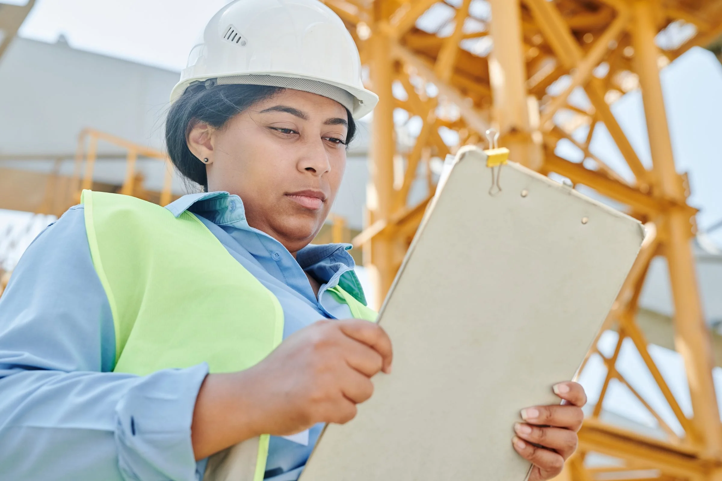Site engineer in hard hat and hi-vis reading a clipboard, crane behind