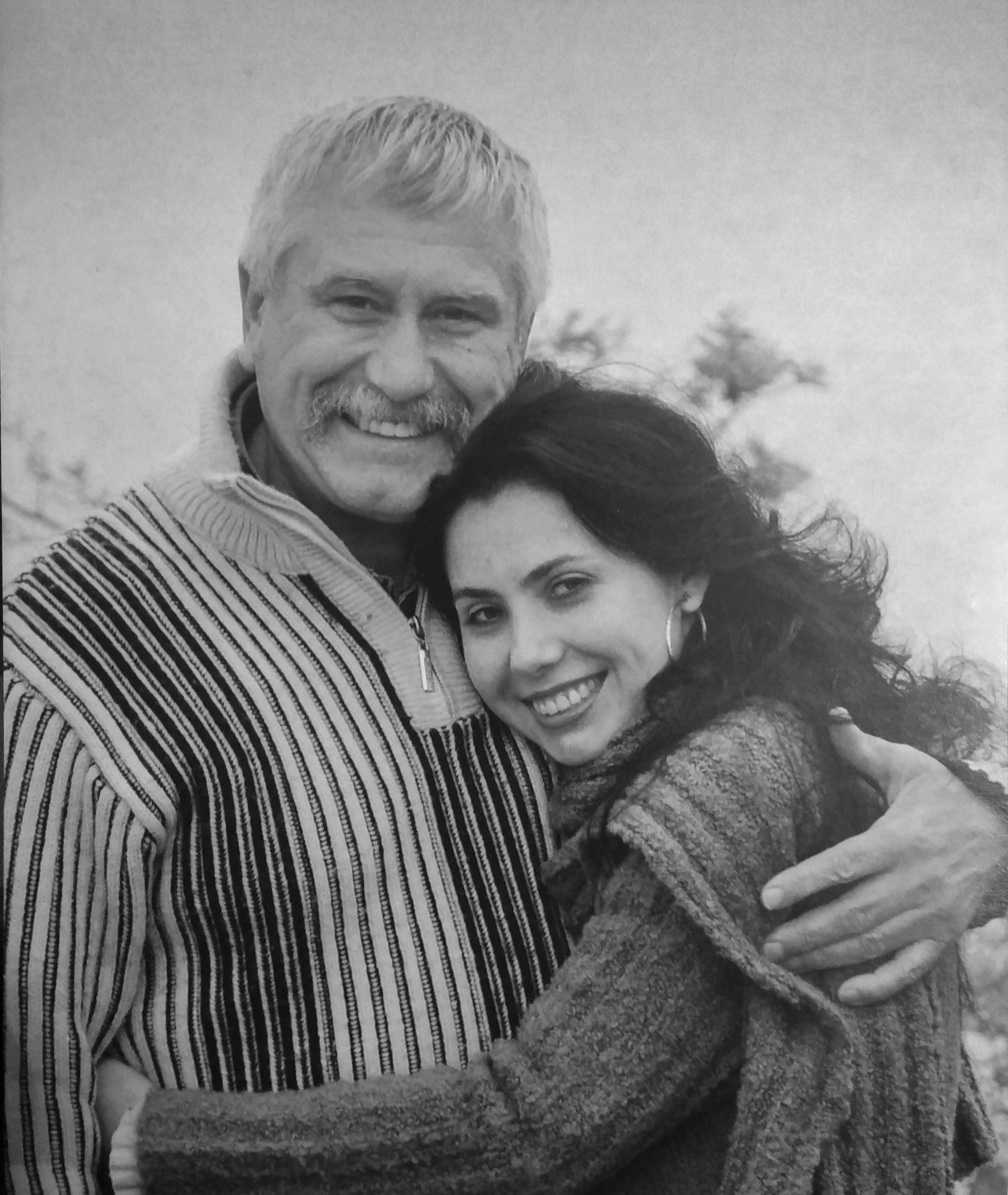 A black-and-white photo of a smiling father embracing a daughter, outdoors with trees in the background.