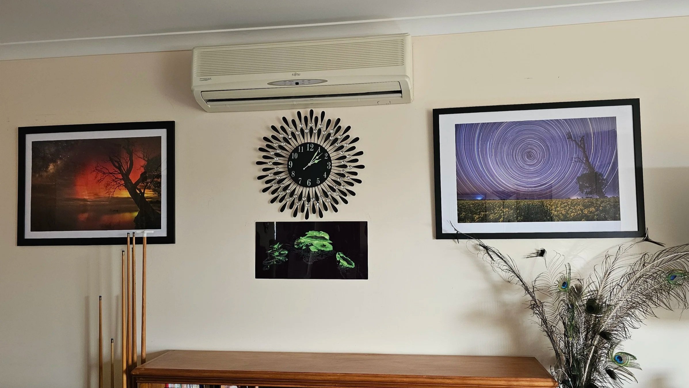 Living room wall with framed nightscape and star trail photographs, a decorative clock, and a Ghost fungi artwork on metal underneath.
