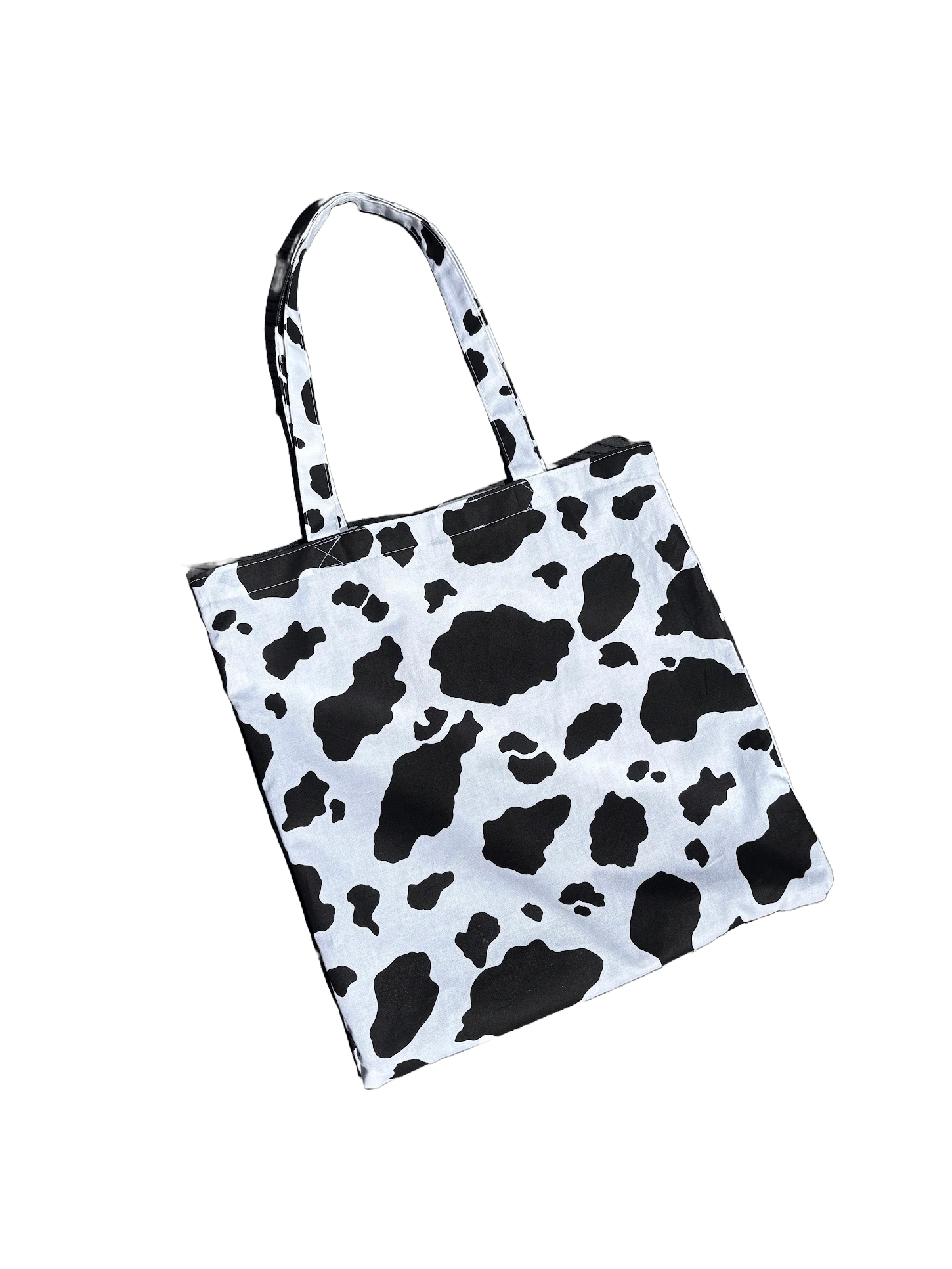 A tote bag with a cow print pattern, featuring black splotches on a white background.