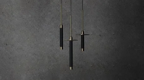 Drei schwarze Hängeleuchten mit goldenen Details hängen vor einer dunklen grauen Wand.