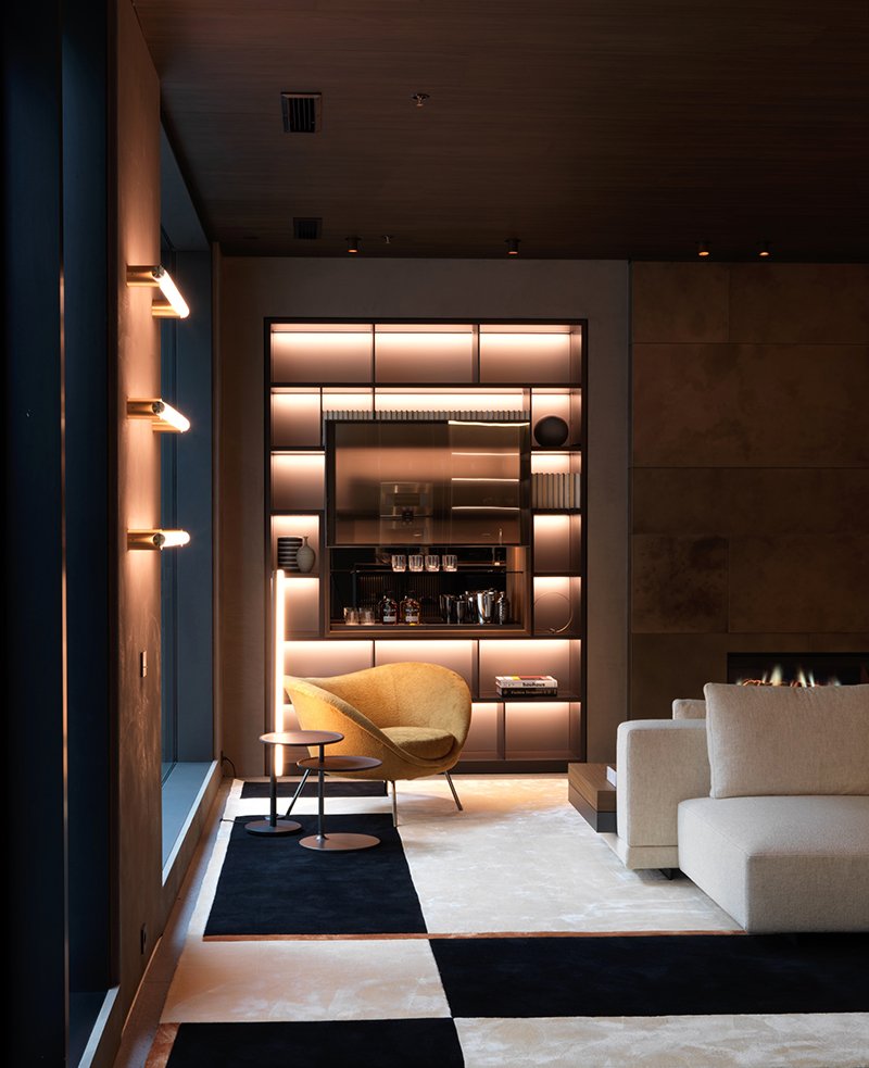 Moderne Wohnzimmerlandschaft mit gemütlicher Sitzecke, beleuchteter Bücherregal, Kamin, geometrischer Teppich, Designer-Stuhl und Tische.