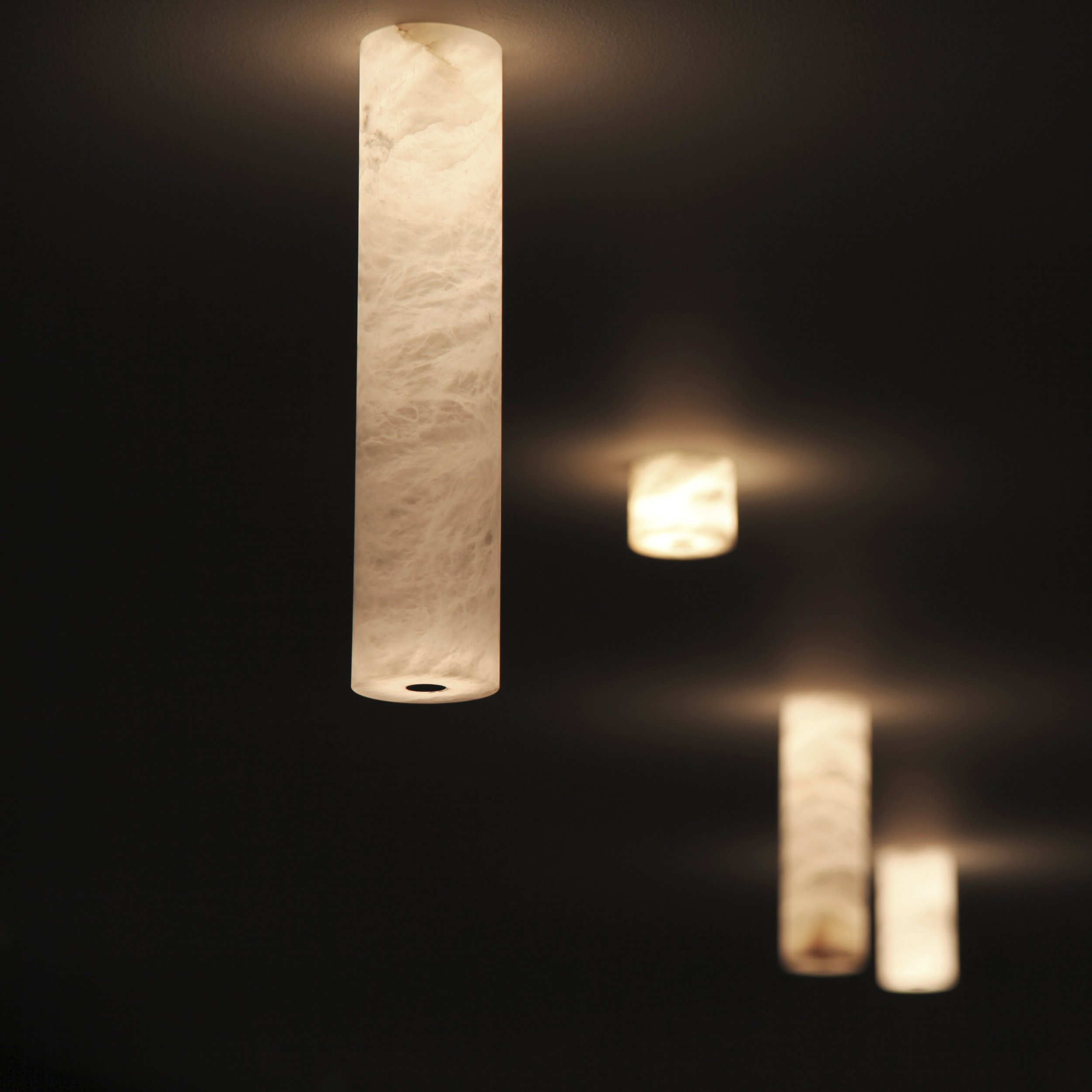 Mehrere hängende Lichtquellen mit warmem Licht, an der Decke in einem dunklen Raum.