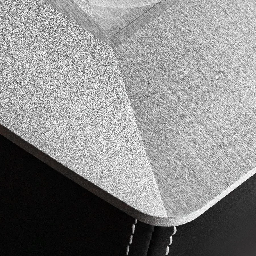 Nahaufnahme der Ecke eines Tisches mit zwei unterschiedlichen Oberflächen, einer glatten weißen und einer grauen mit Muster, und einem schwarzen Stoff darunter.