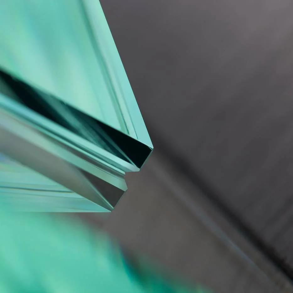 Nahaufnahme von transparentem, bläulichem Glas mit spiegelnder Oberfläche, schräg positioniert vor einem dunklen Hintergrund.