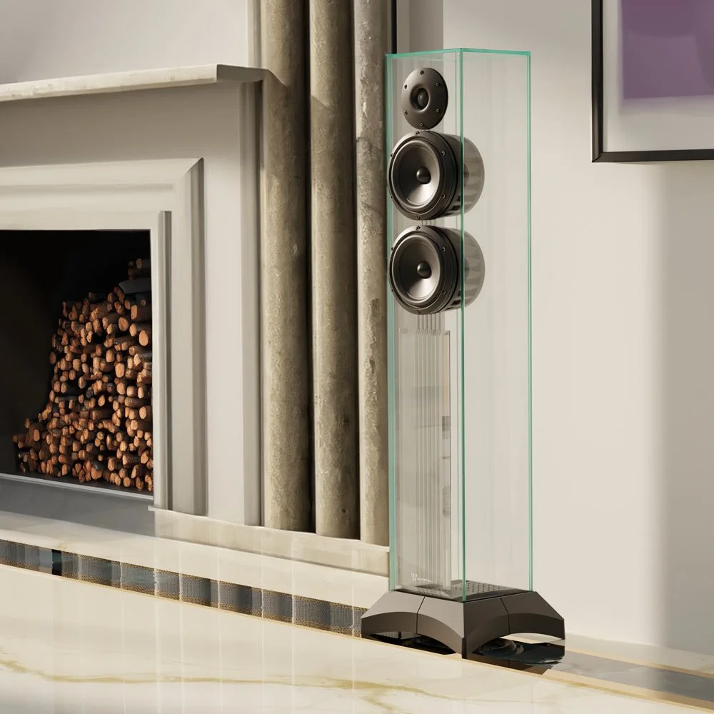 Ein moderner Lautsprecher in einem Glaskasten steht neben einem Kamin mit Holzstapeln.