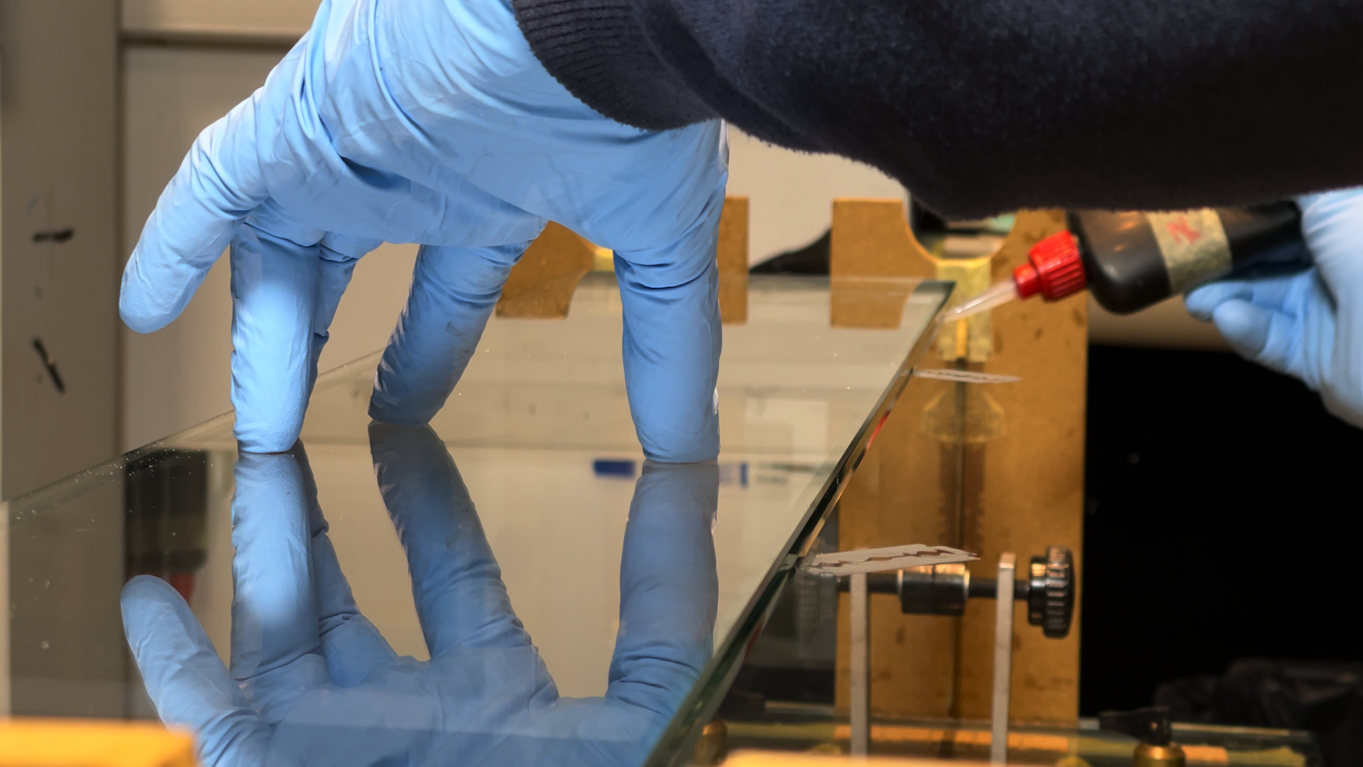Ein Waterfall Audio Mitarbeiter trägt blaue Handschuhe und verwendet eine Pipette, um Flüssigkeit auf eine optische Platte oder Glasplatte zu übertragen. Ein Waterfall Audio Lautsprecher entsteht.