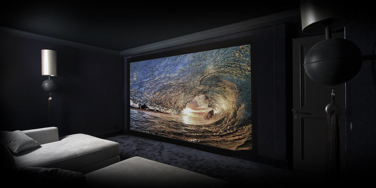 Ein dunkler Wohnraum mit einer großen Leinwand, die eine Welle im Ozean bei Sonnenuntergang zeigt.