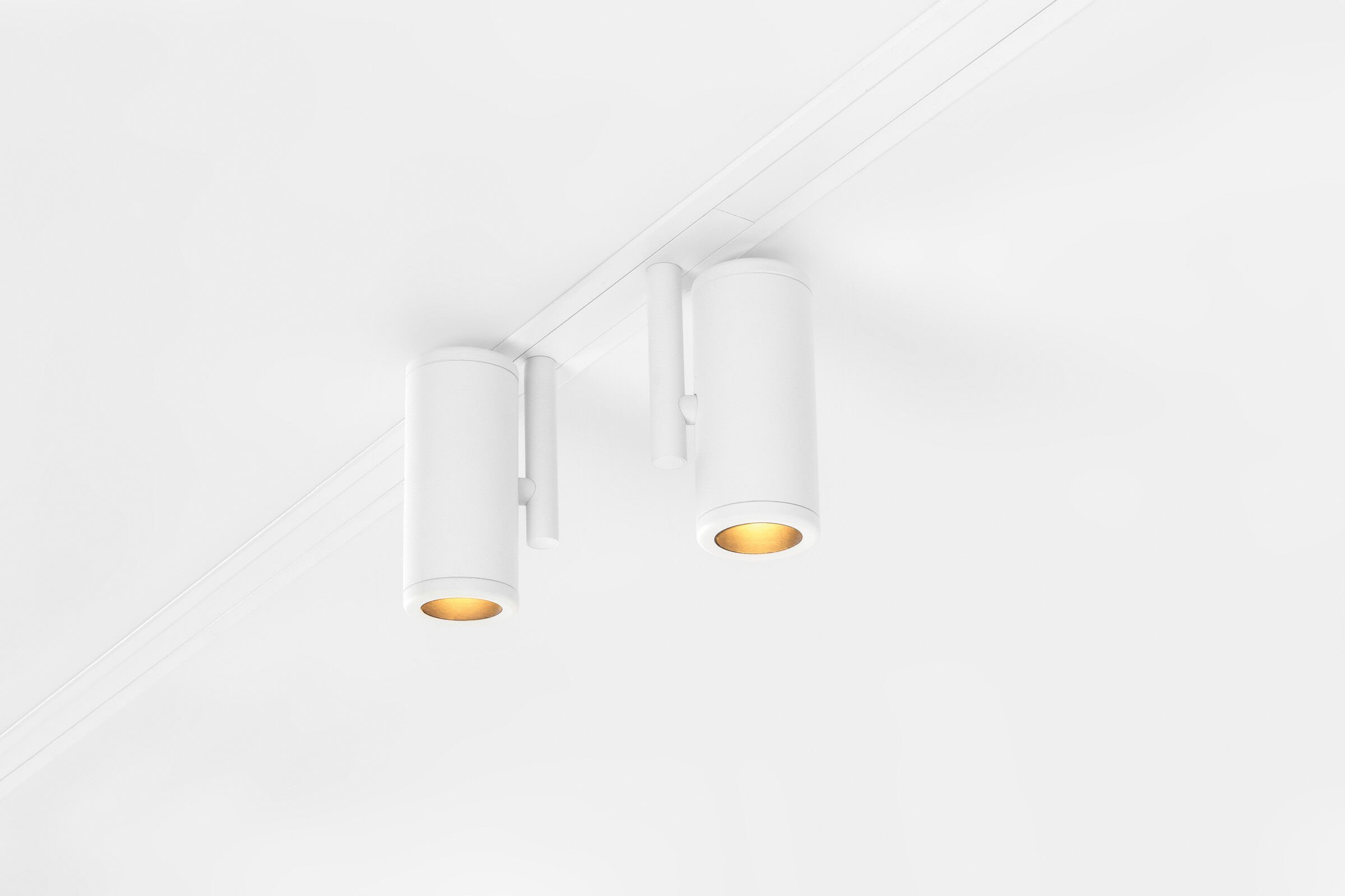Deckenleuchte mit drei weißen, zylindrischen Lampen, die an einer weißen Decke angebracht sind, mit goldenem Licht nach unten strahlend.