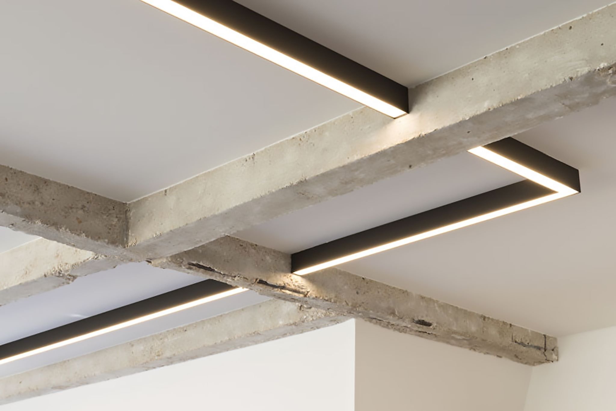 Decke mit sichtbaren Betondeckenbalken und modernen linearen LED-Leuchten.