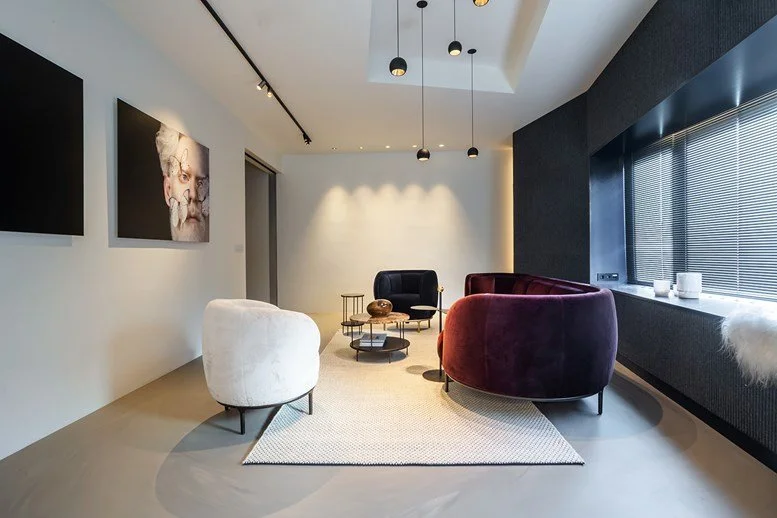 Modernes Wohnzimmer mit weißen und dunklen Möbeln, Wandkunst und großen Fenstern mit Jalousien.