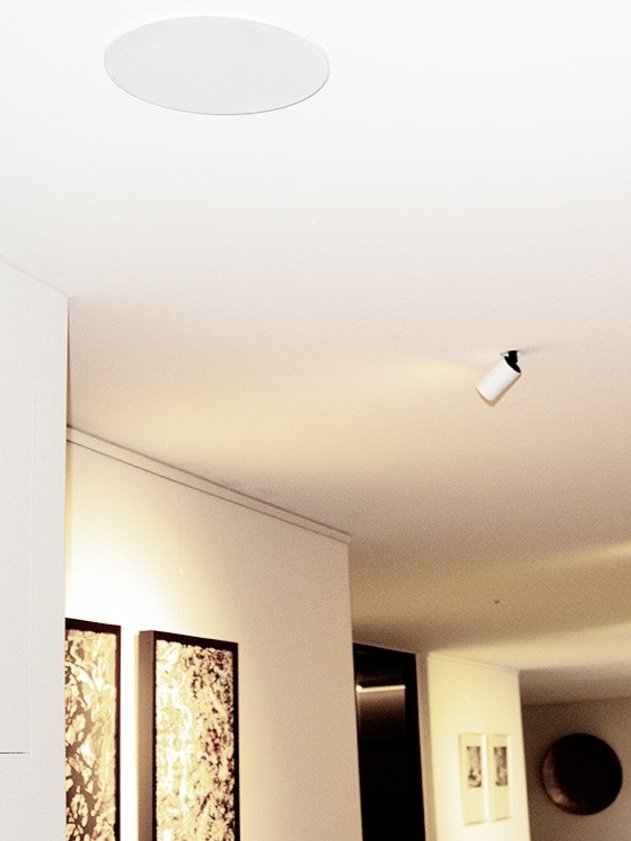 Innenansicht eines Zimmers mit weißen Wänden, Bildern an der Wand, Deckenleuchte und Track-Licht