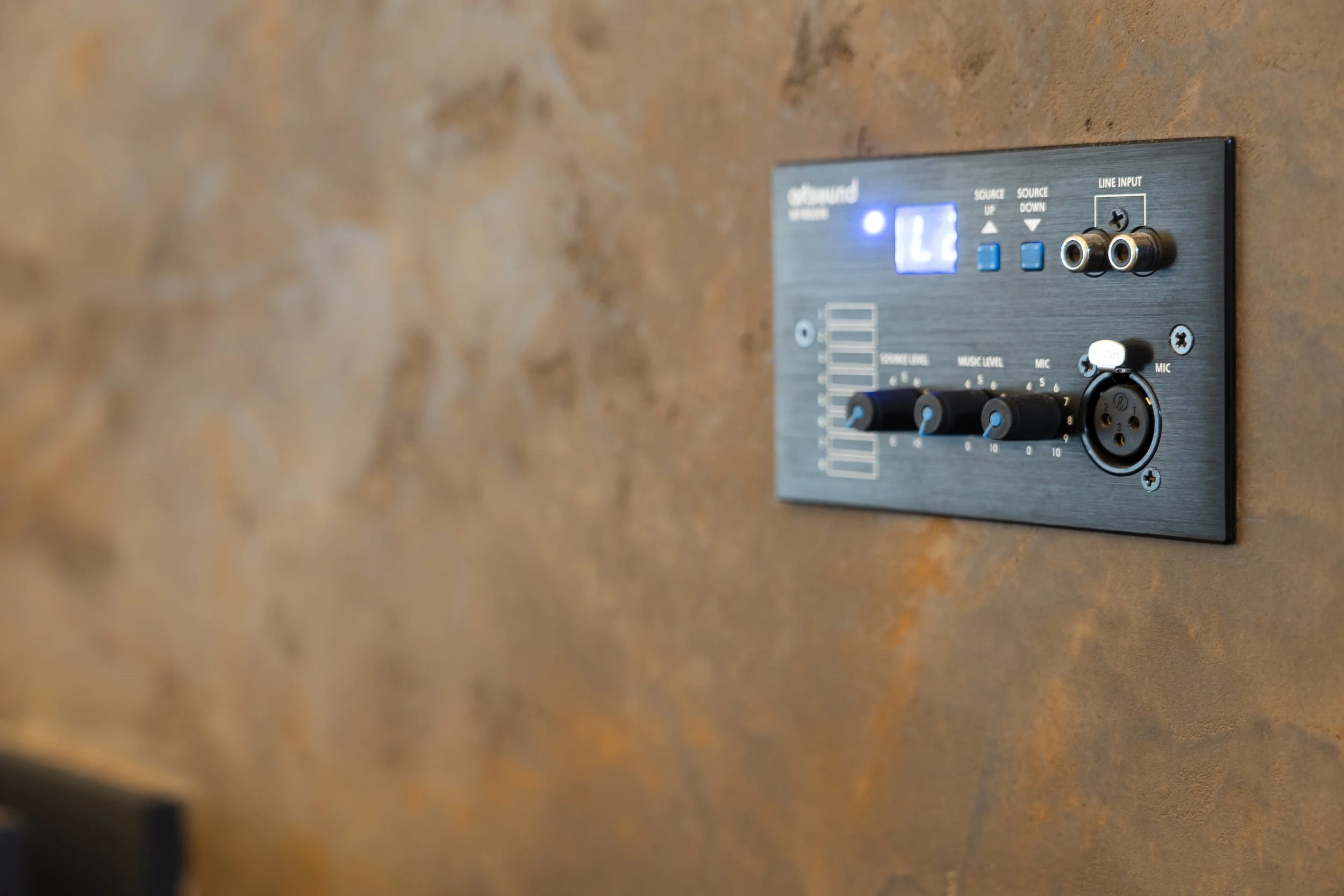 Ein audio-steuerpanel mit Reglern, Anschlüssen und einem digitalen Display an einer Wand aus braun-orangefarbenem Material.