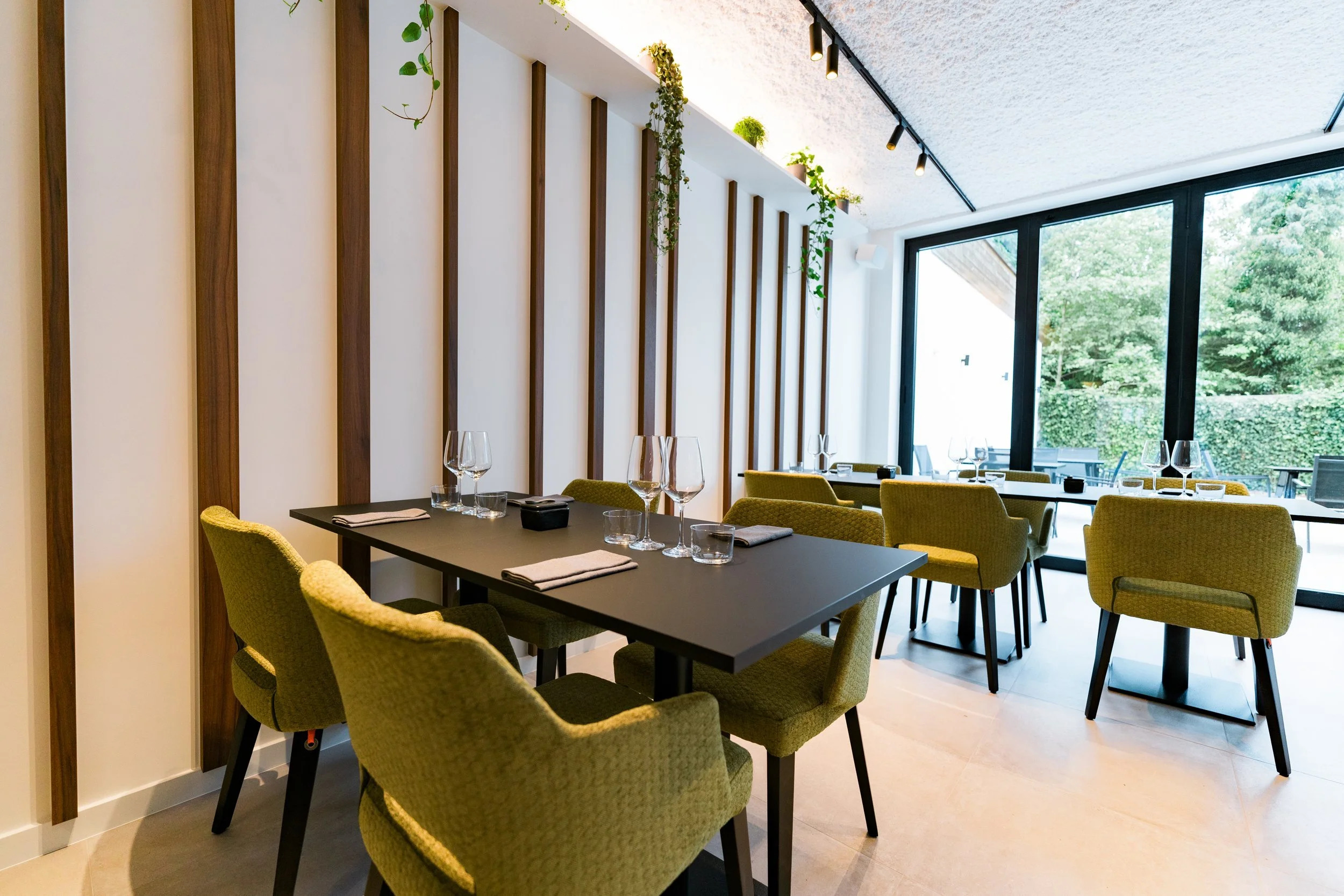 Eleganter, moderner Restaurantraum mit grünen Sesseln, Wein- und Wassergläsern auf schwarzen Tischen, große Fenster mit Blick nach draußen