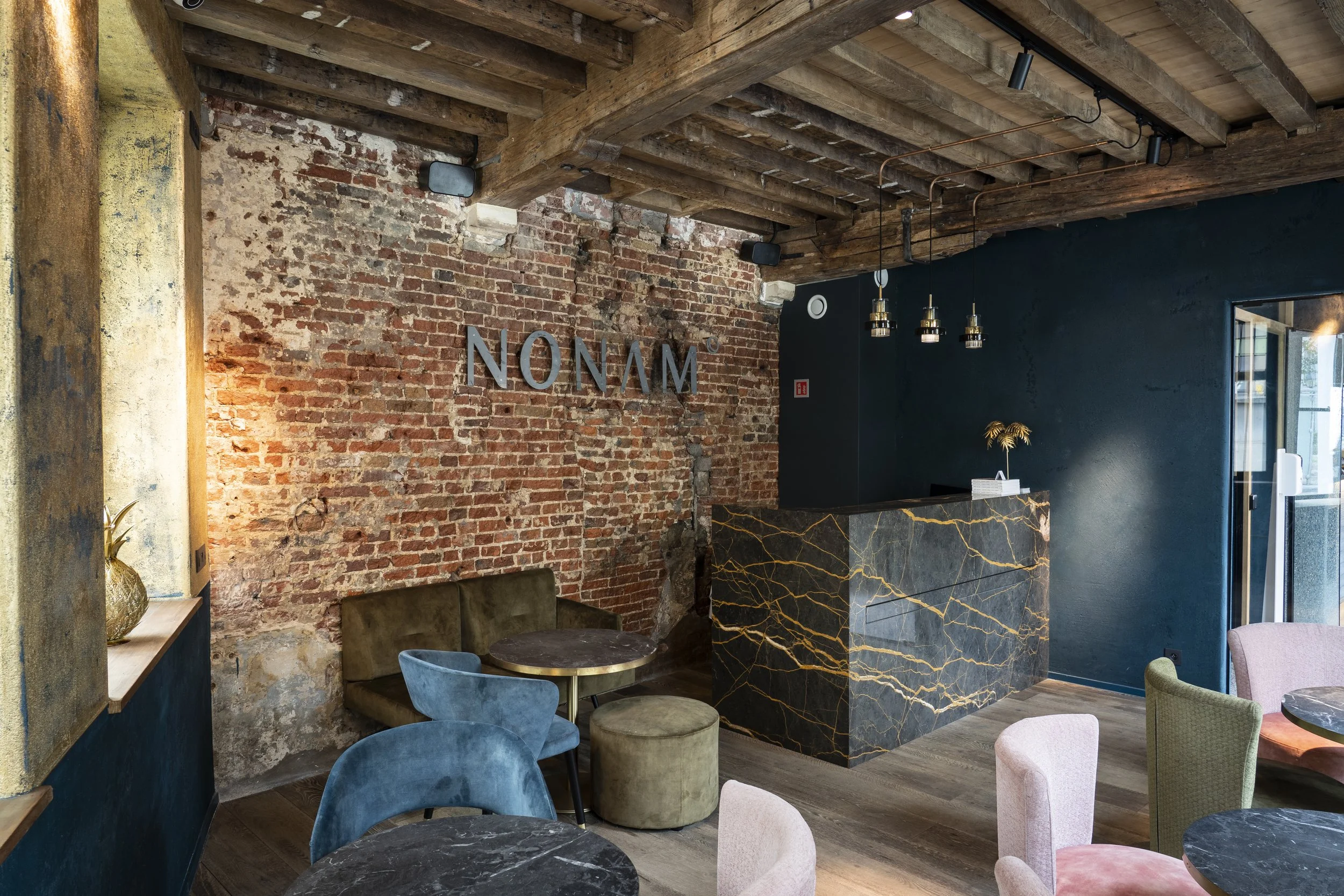 Inneneinrichtung eines Cafés mit braunen Ziegelwänden, dunklem blauen Wand, einem schwarzen Marmortresen mit goldenen Adern, mehreren bunten Sesseln und einem Holzdeckenboden.