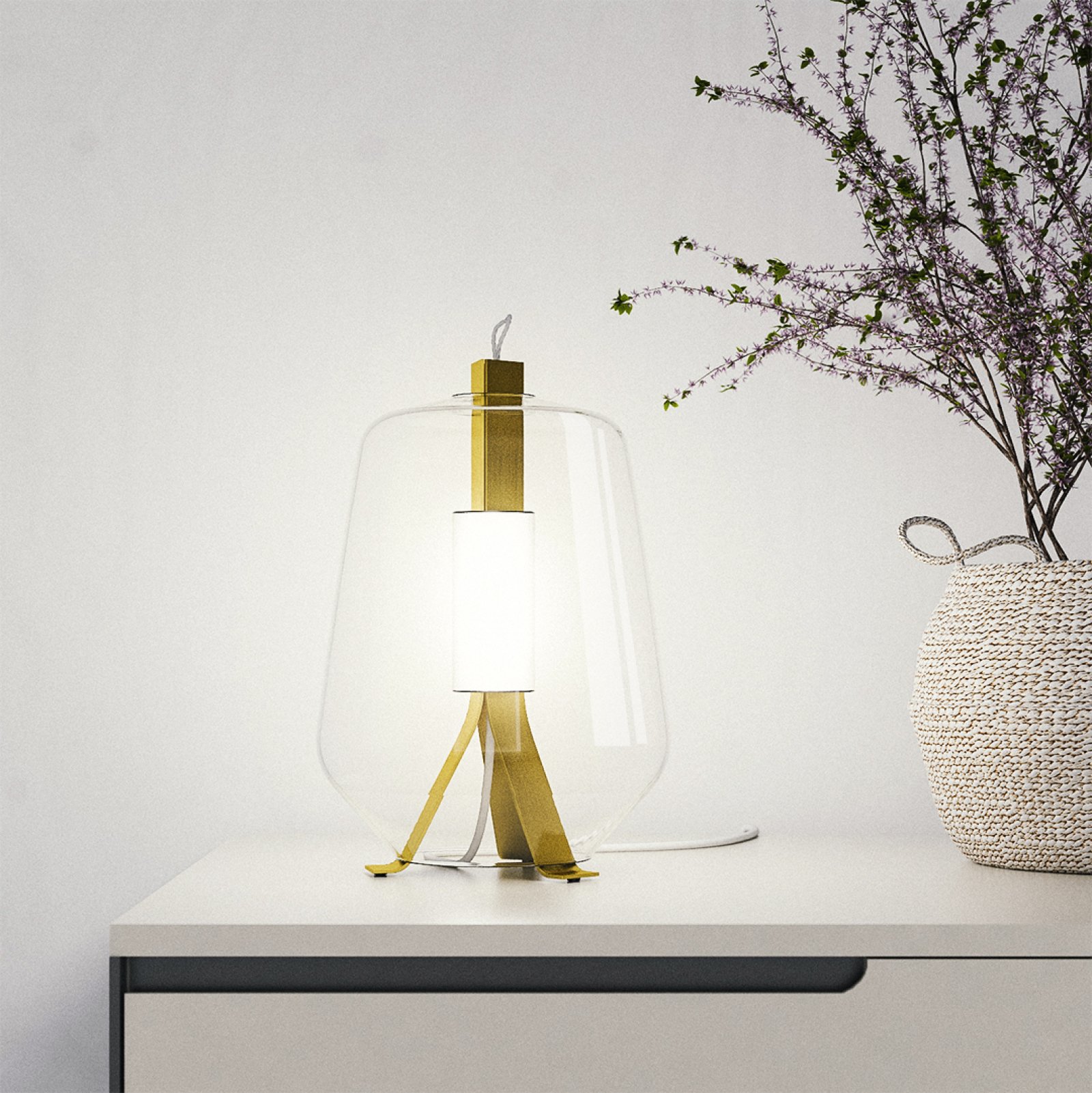 Moderne Tischlampe mit goldenem Gestell und weißem Lampenschirm auf einem weißen Tisch neben einem Korb mit einer Pflanze.