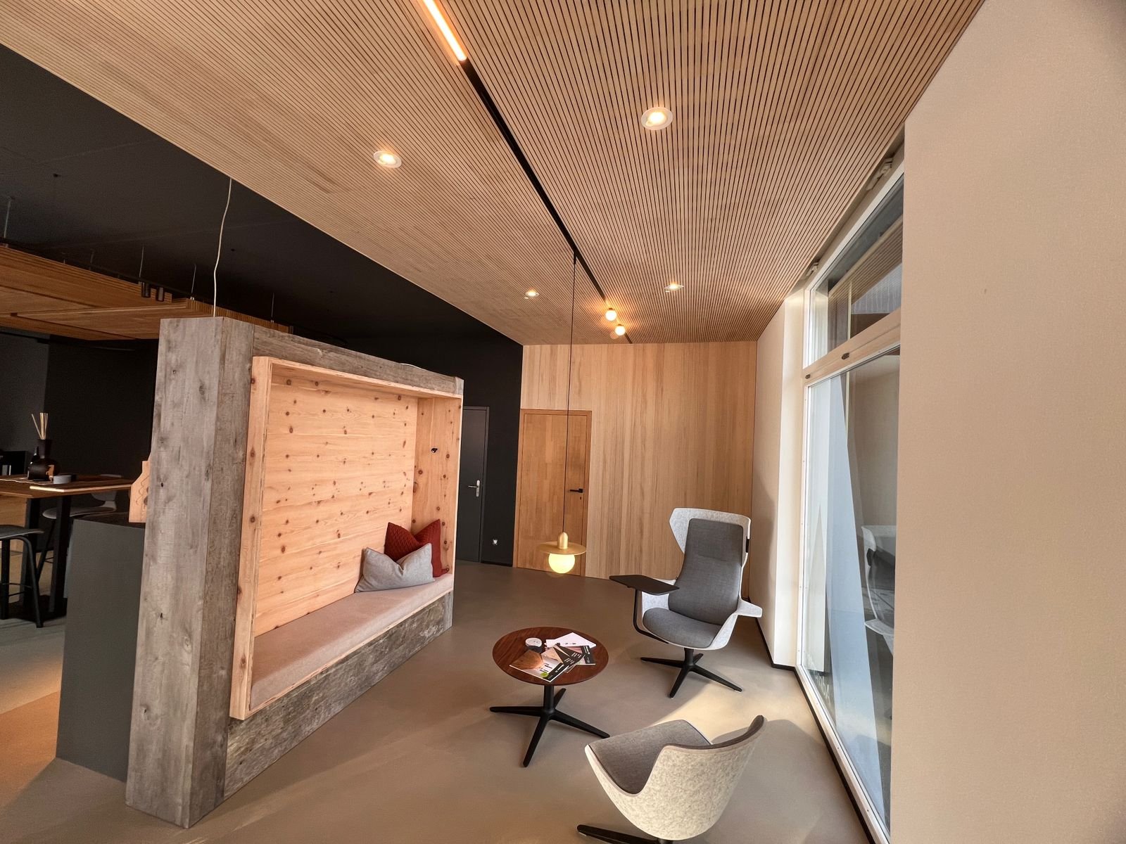 Modernes Wohnzimmer mit Holzwand, bequemen Sesseln, großem Fenster und Holzdecke mit eingebauten Lichtern.