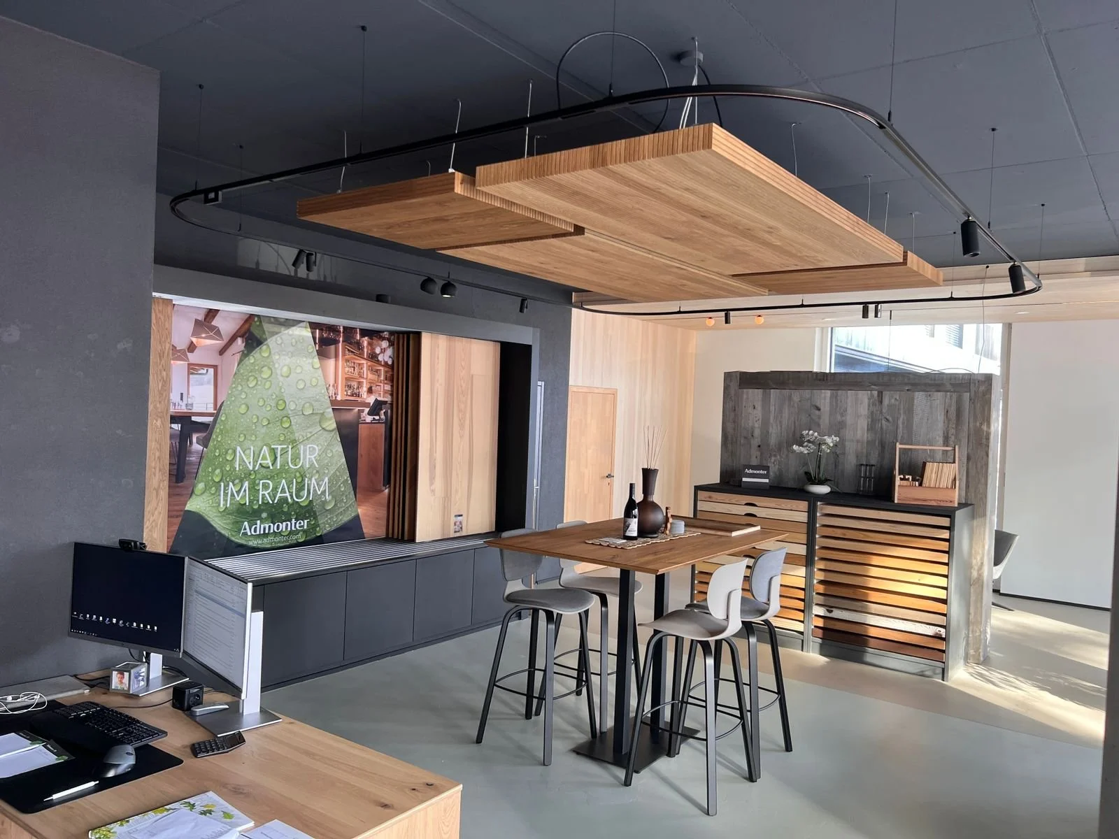 Modernes Büro mit Holzdekoration, Stehtisch, Barhockern und großem Bildschirm mit dem Text "NATUR IM RAUM".
