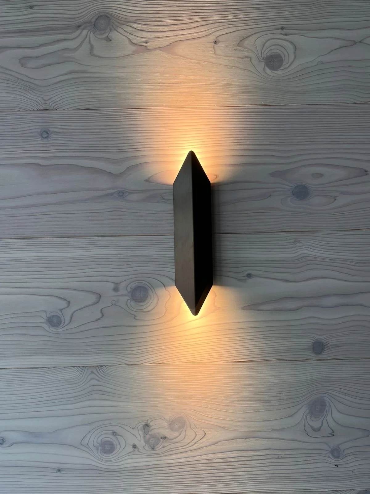 Ein langes, dünnes, schwarzes Gegenstand, der auf einer beleuchteten Holzoberfläche liegt, die mit sichtbaren Holzmaserungen und Knoten versehen ist. Das Licht scheint von oben und unten, wodurch der Gegenstand einen Schatten auf die Oberfläche wirft