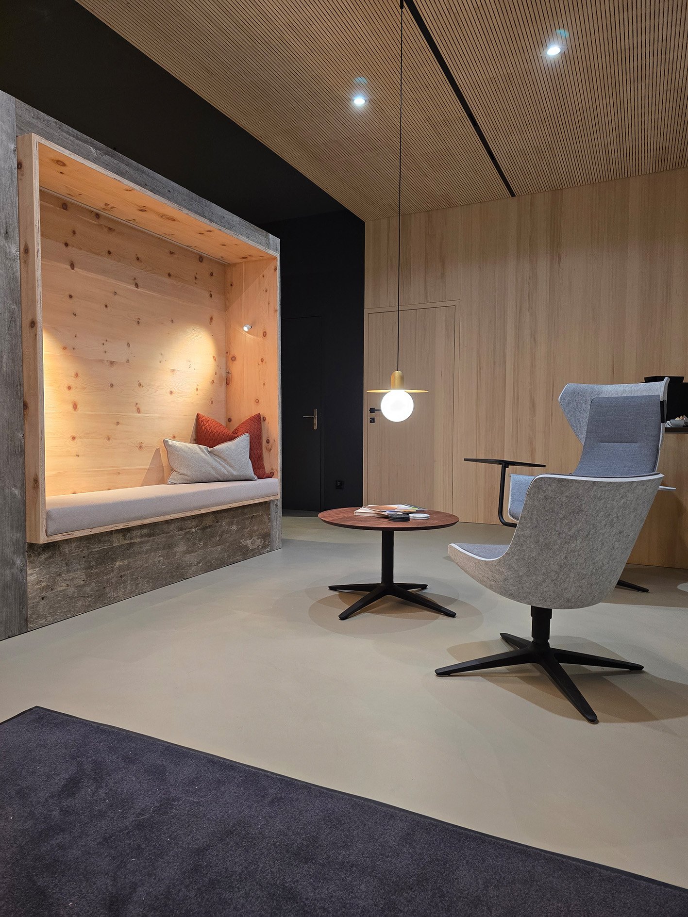 Gemütlicher Loungebereich mit einem Sitznische mit Polsterung, zwei modernen Stühlen, einem kleinen runden Tisch, hängende Deckenlampe und Holzverkleidungen an Wand und Decke.