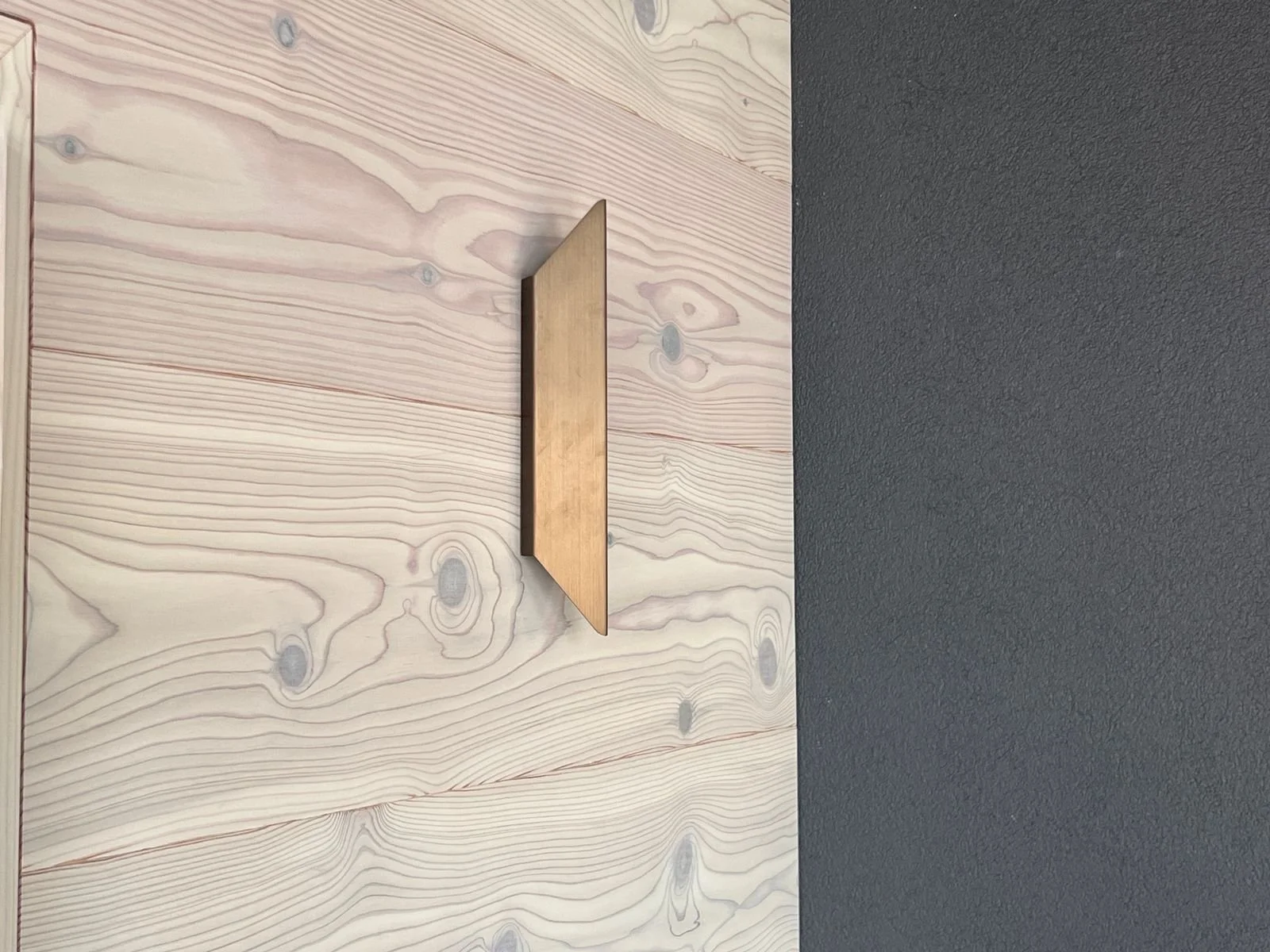 Ein Holzschild an einer Wand, die zur Hälfte aus Holz und zur Hälfte aus glatter, heller Wand besteht.