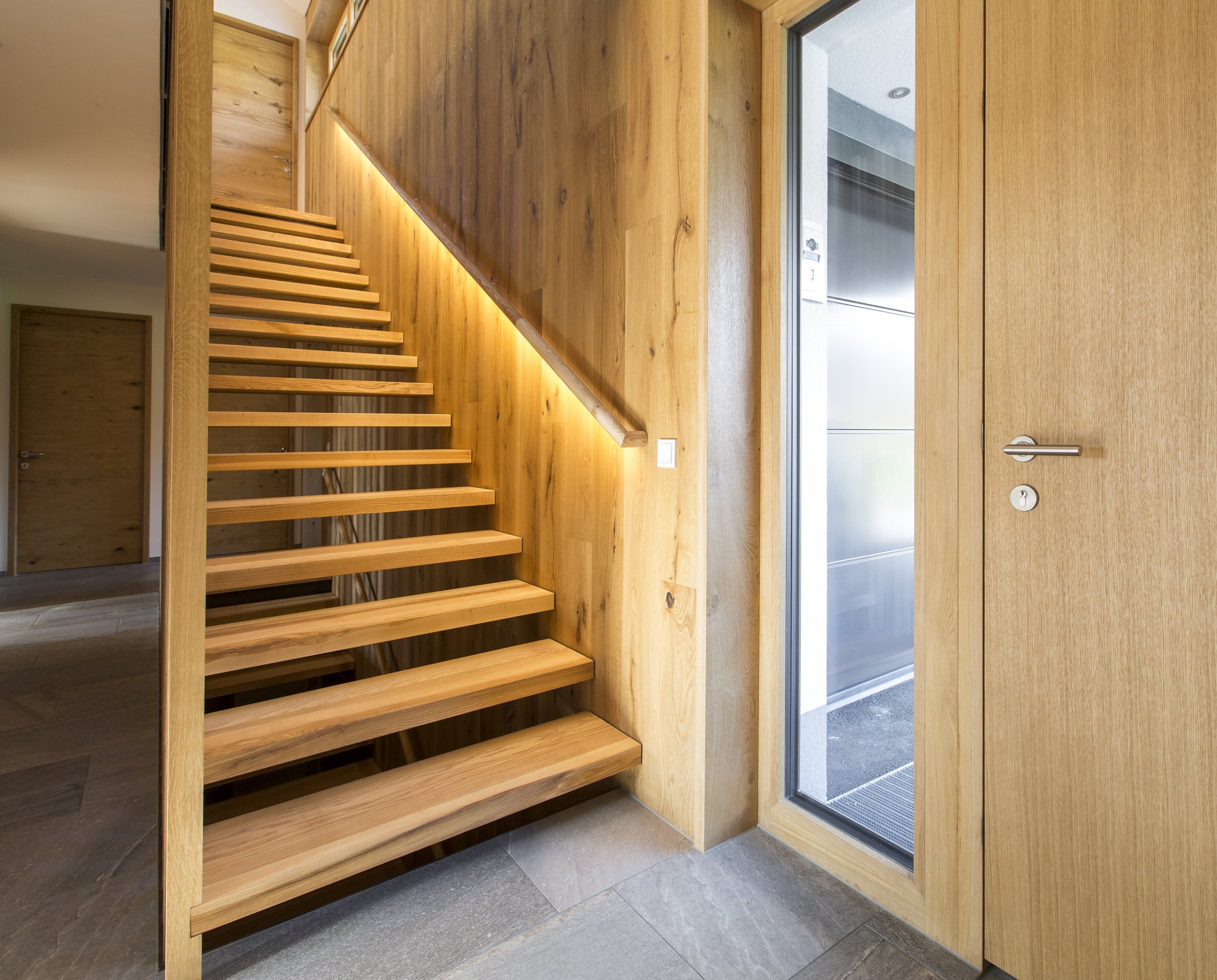 Innenansicht eines Hauses mit Holztreppe, Holz- und Glastüren, modernem Design, dunklem Boden