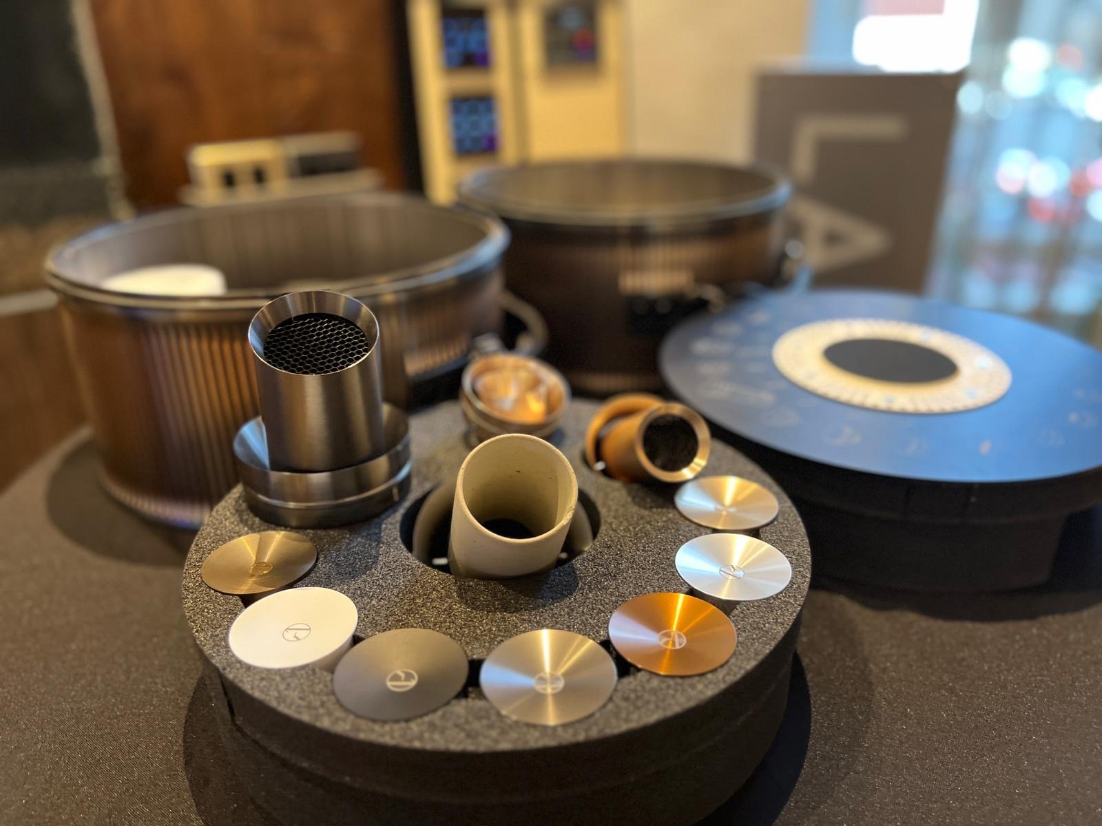 Zubehör für die Zubereitung von Kaffee, einschließlich einer Kaffeekanne, Mahlwerk, Messbecher, Kaffeemühle und Zubehörteile auf einer schwarzen Oberfläche.