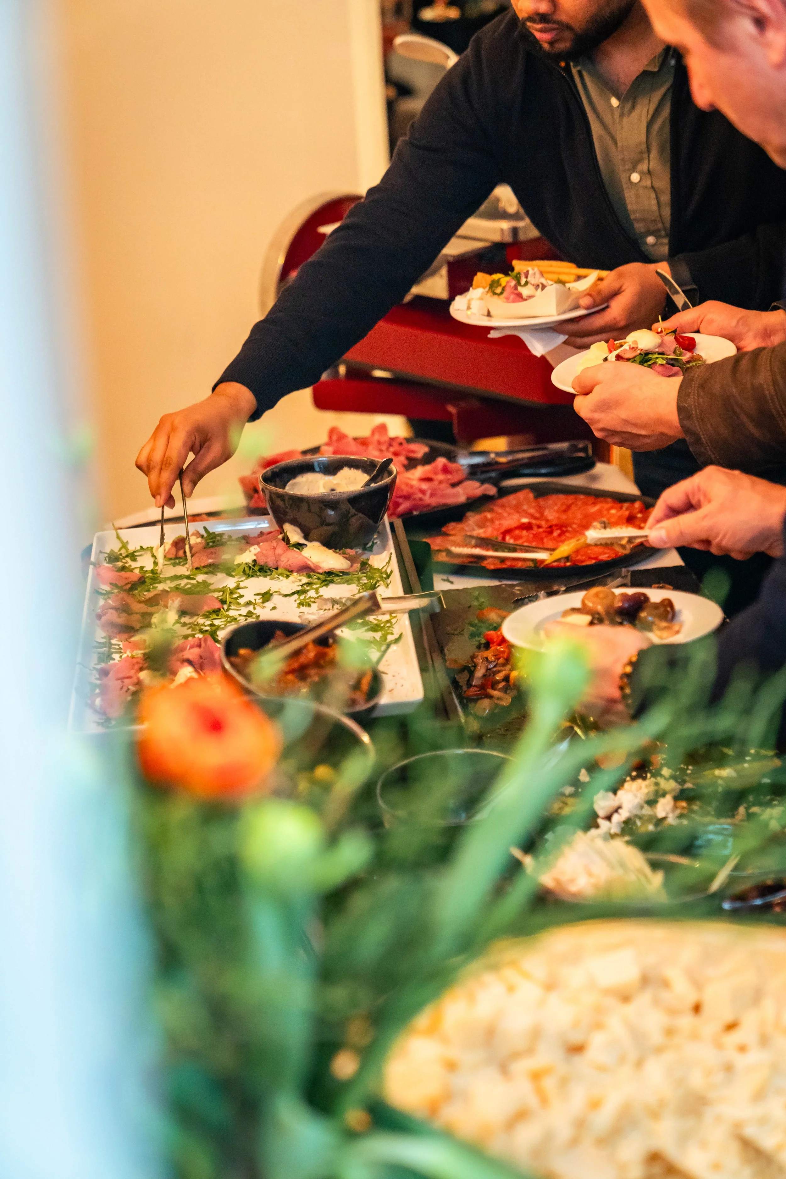 Menschen nehmen Speisen von einem Buffet mit verschiedenen Fleisch- und Gemüsegerichten auf Tellern