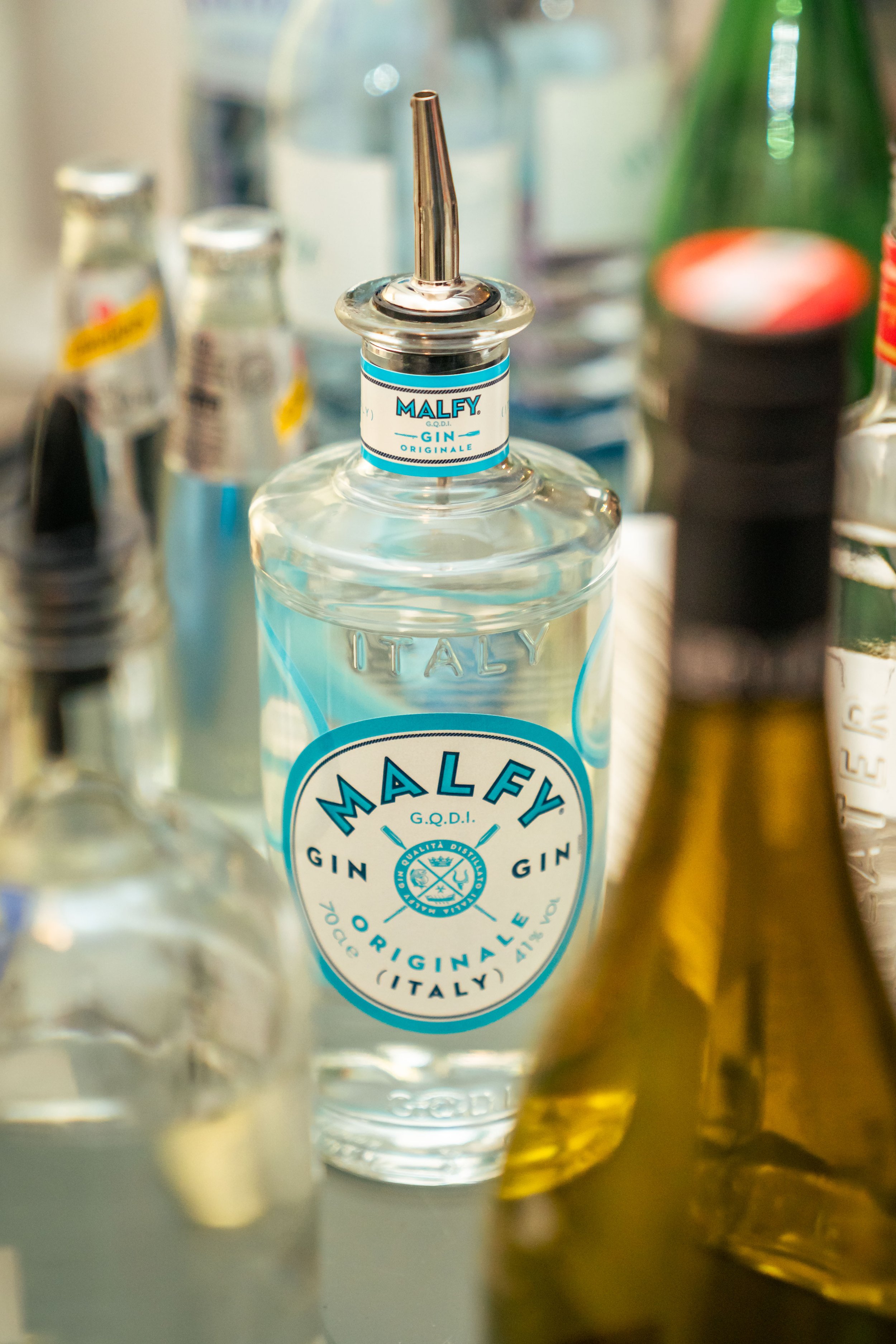 Flasche Gin mit blauer und weißer Beschriftung, umgeben von anderen Flaschen und Gläsern