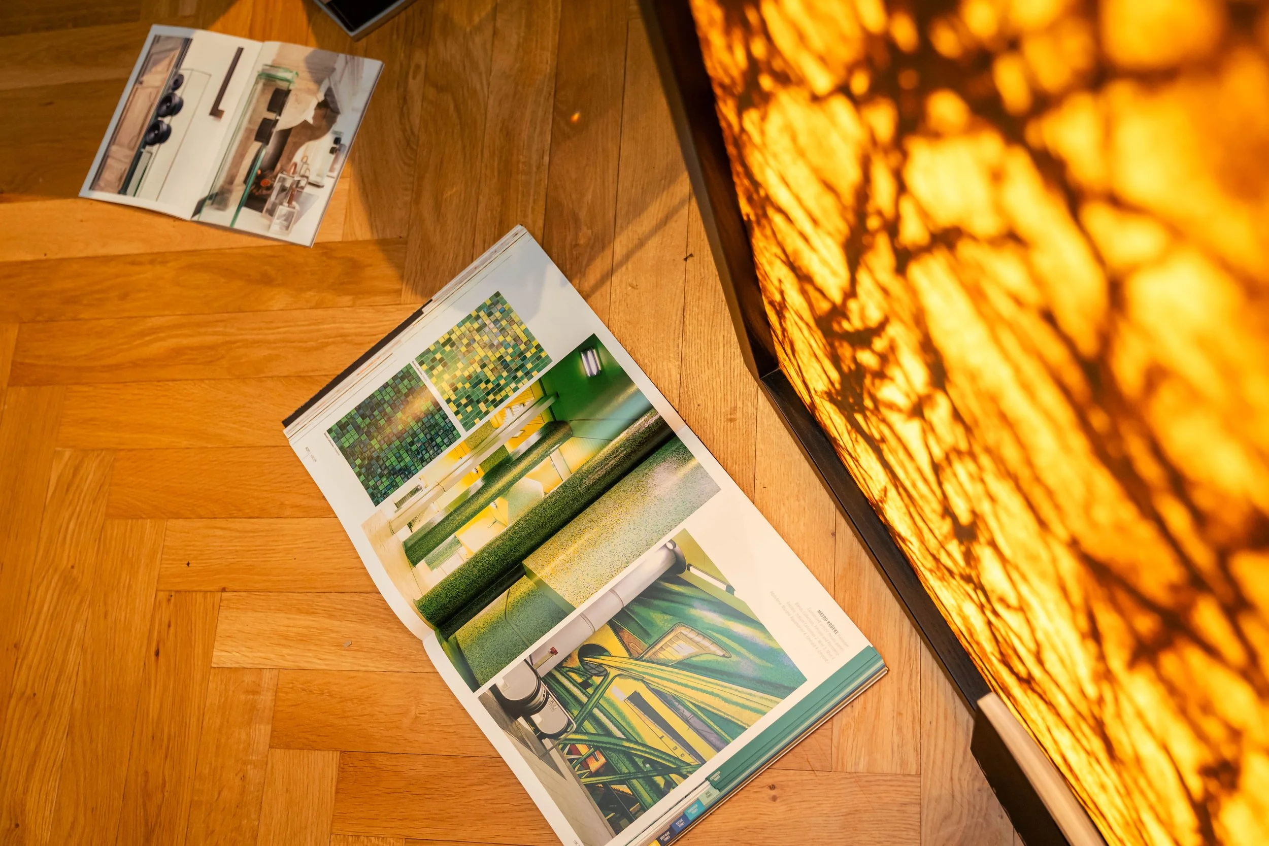 Offener Kunst- oder Designkatalog auf einem Holztisch, mit Farbmuster und technischen Skizzen, neben einem Bildschirm, der ein orange-gestreiftes Muster zeigt.