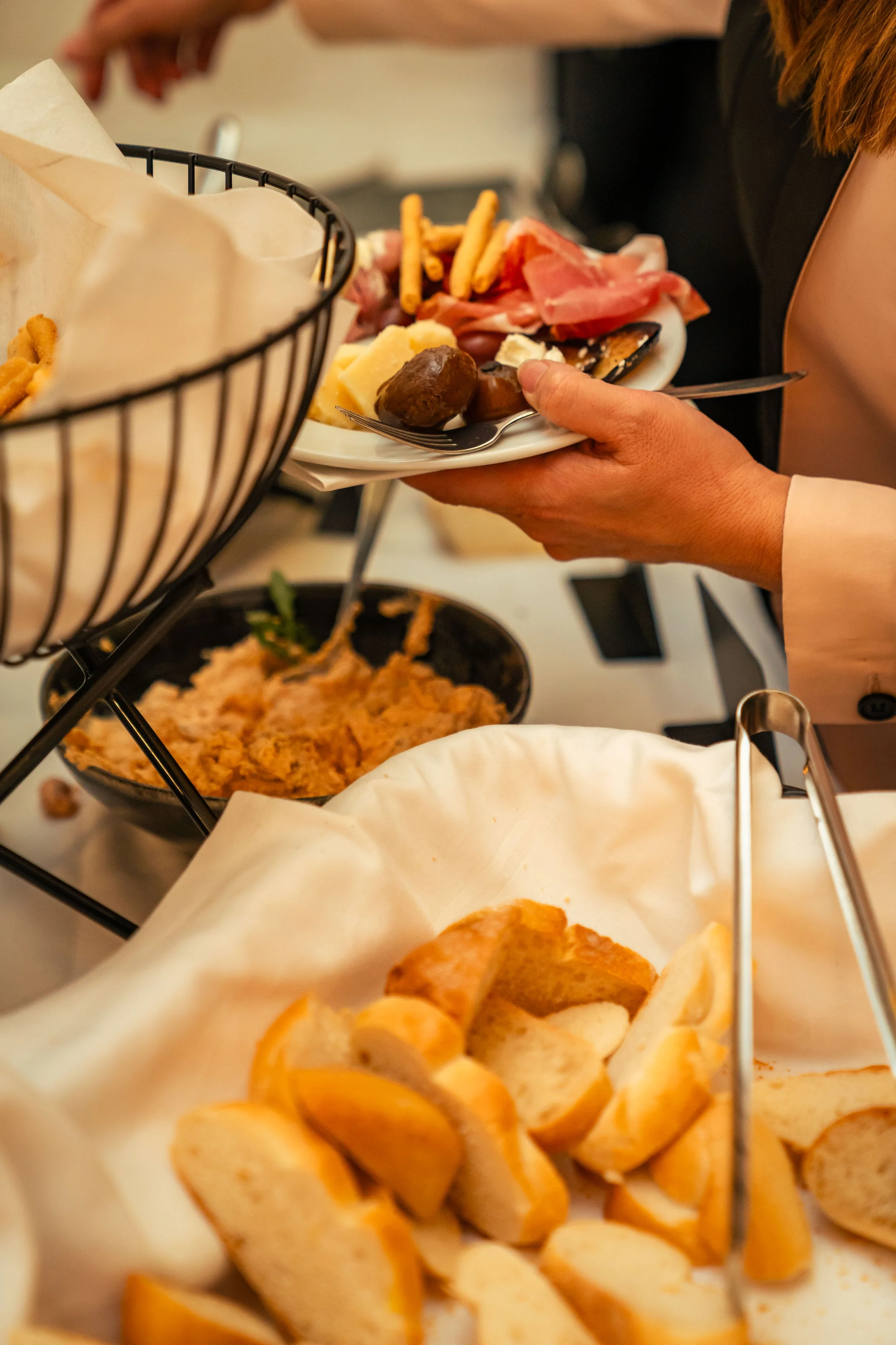 Person beim Essen eines Buffets mit Fleisch, Käse, Brot und Desserts.