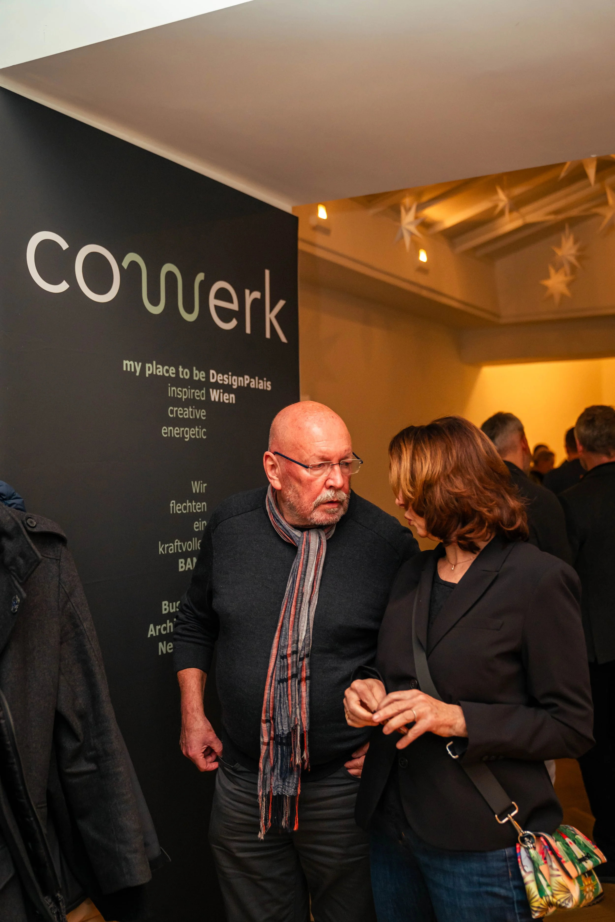 Zwei Personen im Gespräch bei einer Veranstaltung, im Hintergrund eine schwarze Tafel mit dem Wort 'conwerk' und deutschem Text.