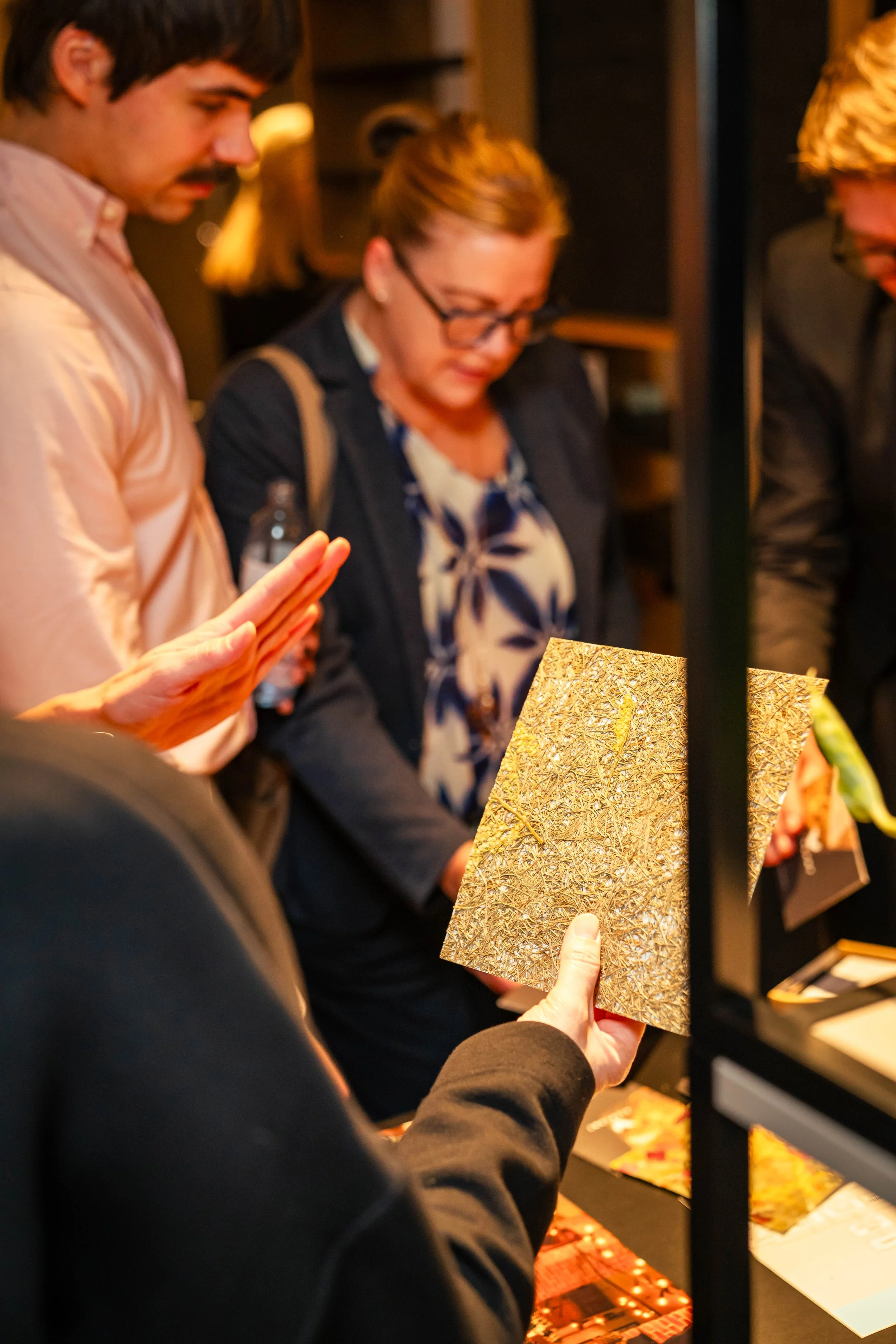 Menschen betrachten kunstvolle, goldfarbene Werke bei einer Ausstellung oder einem Kunstverkauf.
