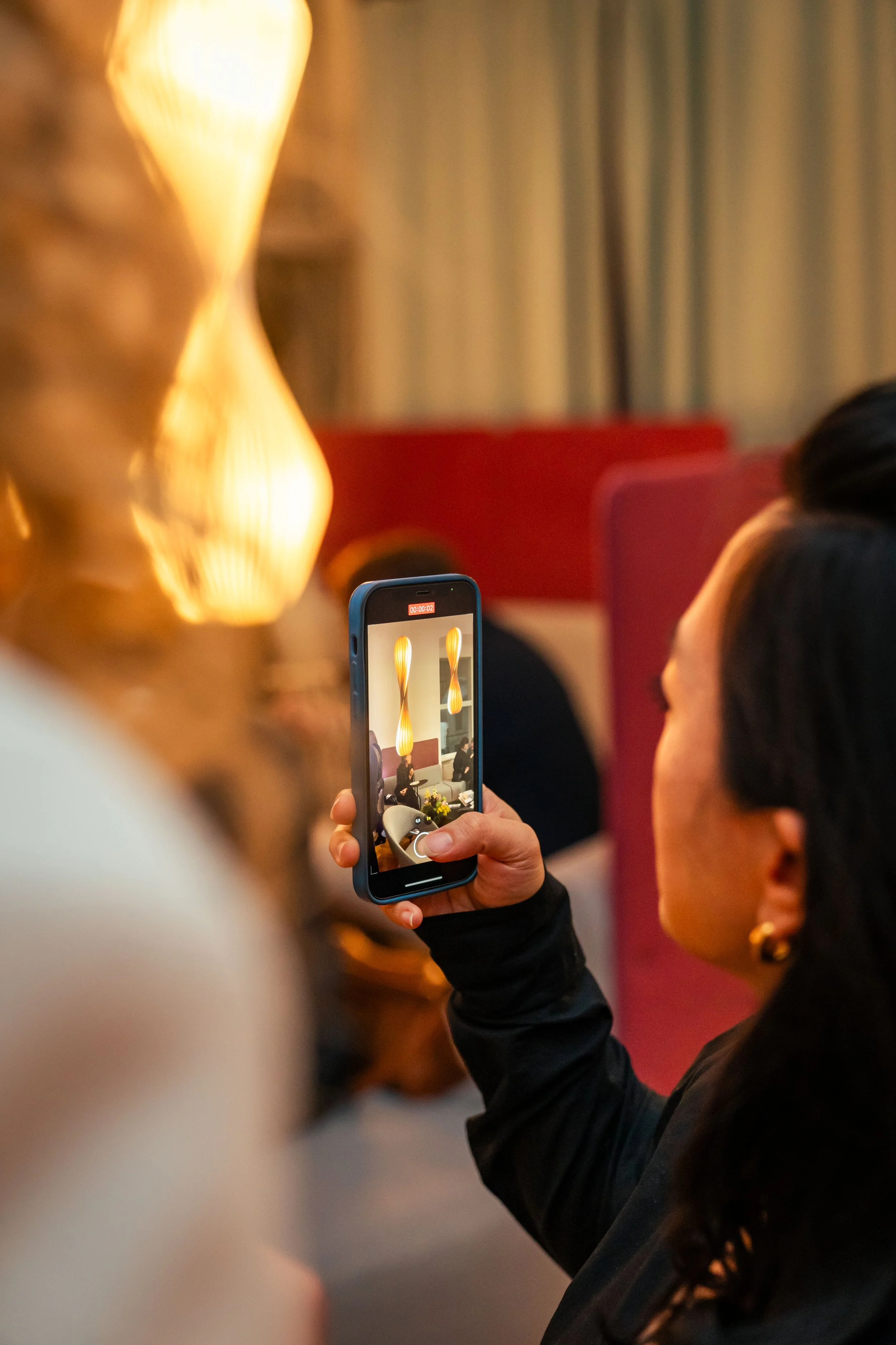 Frau filmt mit dem Smartphone eine große Lampenskulptur in einem stilvollen Raum.