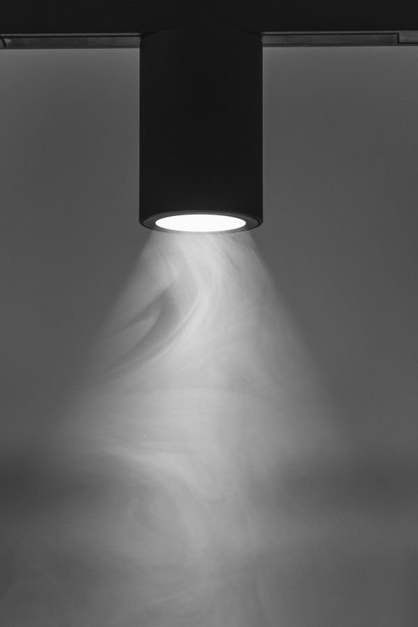 Eine moderne Deckenleuchte strahlt Licht und verteilt feinen Staub oder Nebel im Raum.