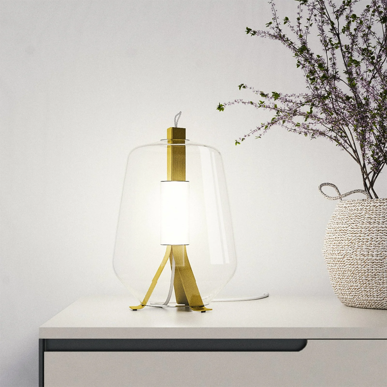 Moderne Tischlampe aus Glas und Metall auf weißem Tisch neben einem Korb mit einer Pflanze