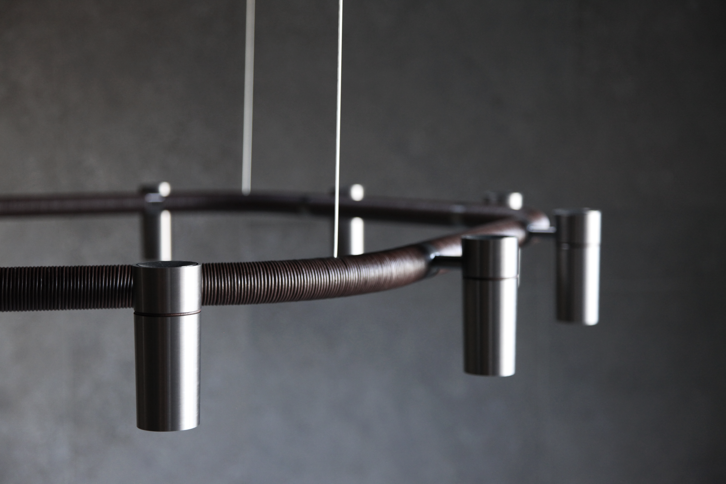Moderne Hängelampe aus Metall mit sichtbaren Schraubteilen an einem dunklen Hintergrund.