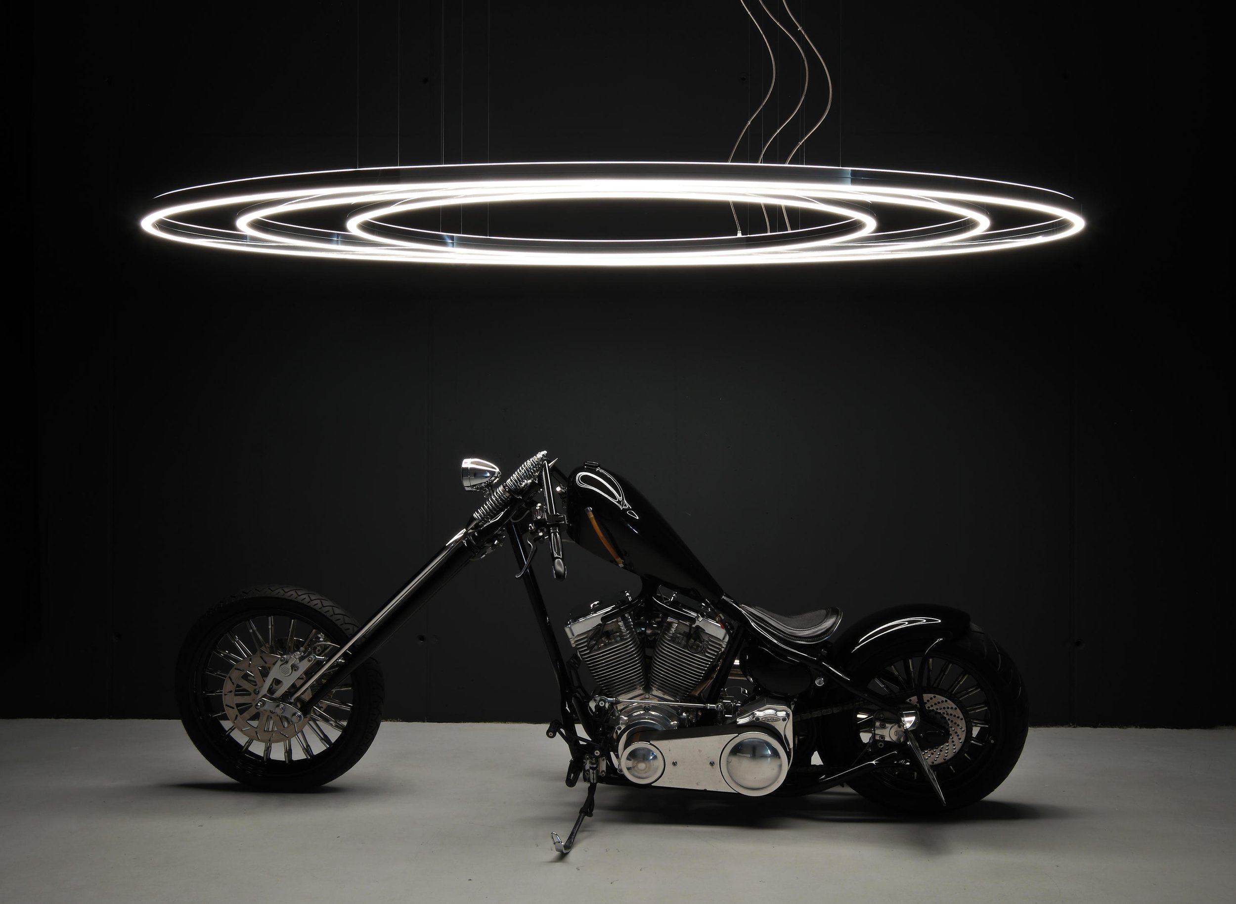 Schwarze Motorrad vor schwarzer Wand, oberhalb leuchtende kreisförmige Neonlichter