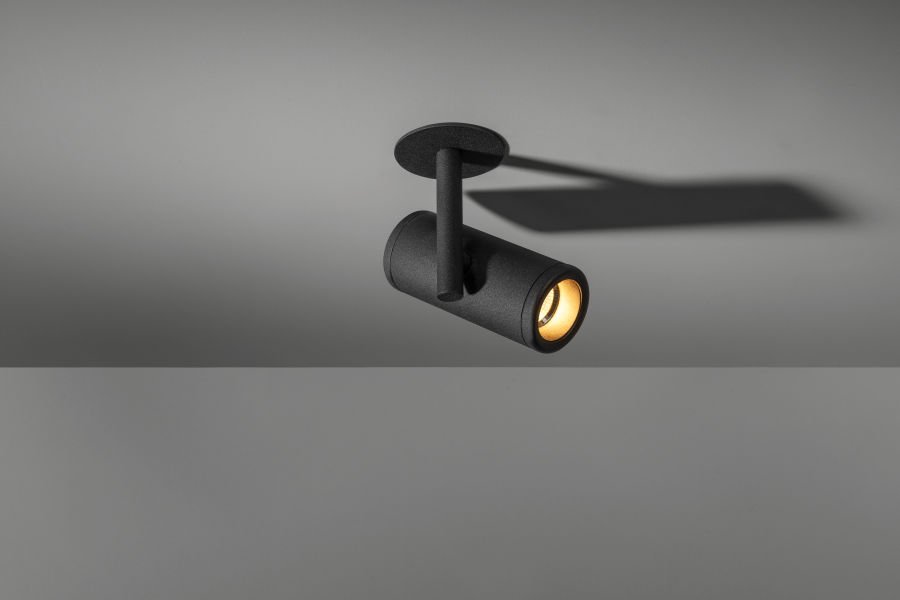 Schwarze Deckenleuchte mit direktem Licht auf einer grauen Wand.