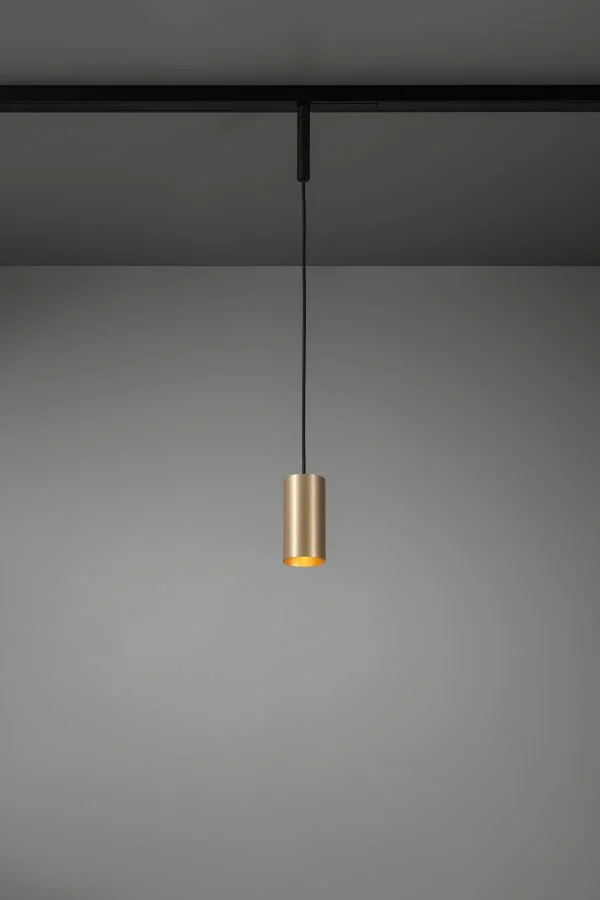 Eine moderne, goldene Pendelleuchte hängt von der Decke an einer schwarzen Schnur vor einer grauen Wand.