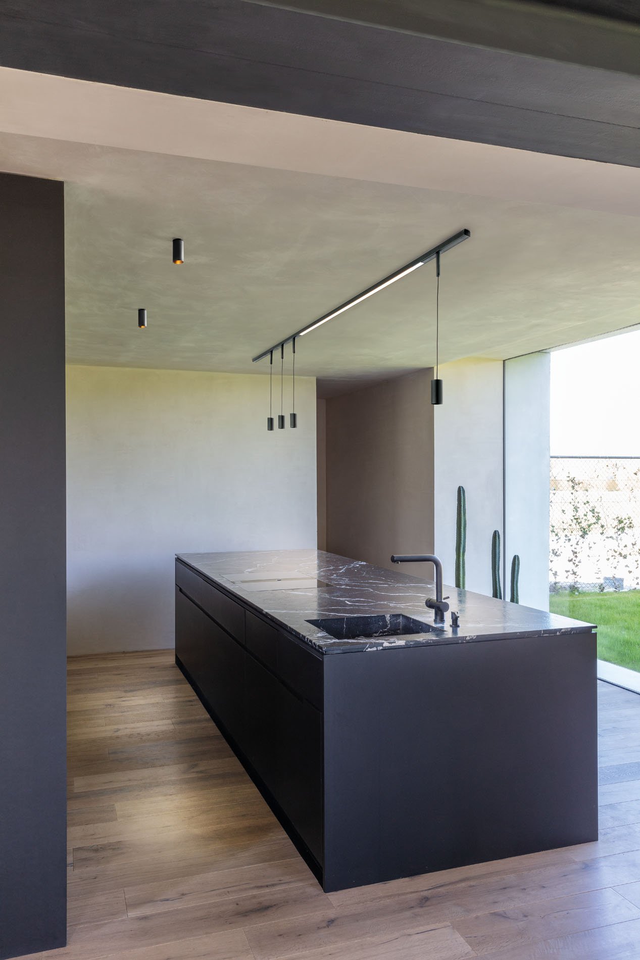 Moderne Küche mit schwarzer Insel aus Marmor, einem sink, Wasserhahn, hängenden schwarzen Leuchten und großen Fenster mit Blick auf den Garten.