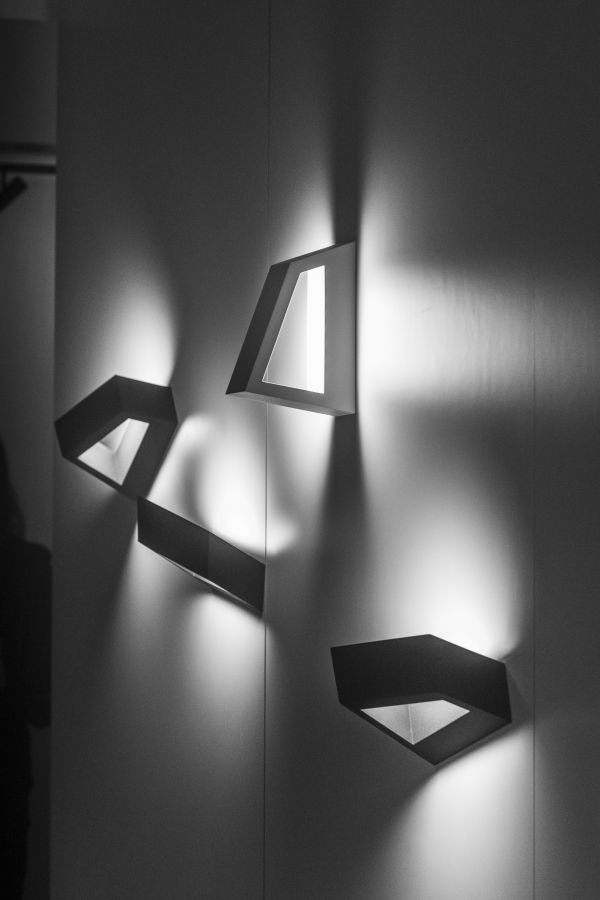 Drei moderne Wandlichter in geometrischem Design, die Licht nach oben und unten auf eine glatte weiße Wand werfen.