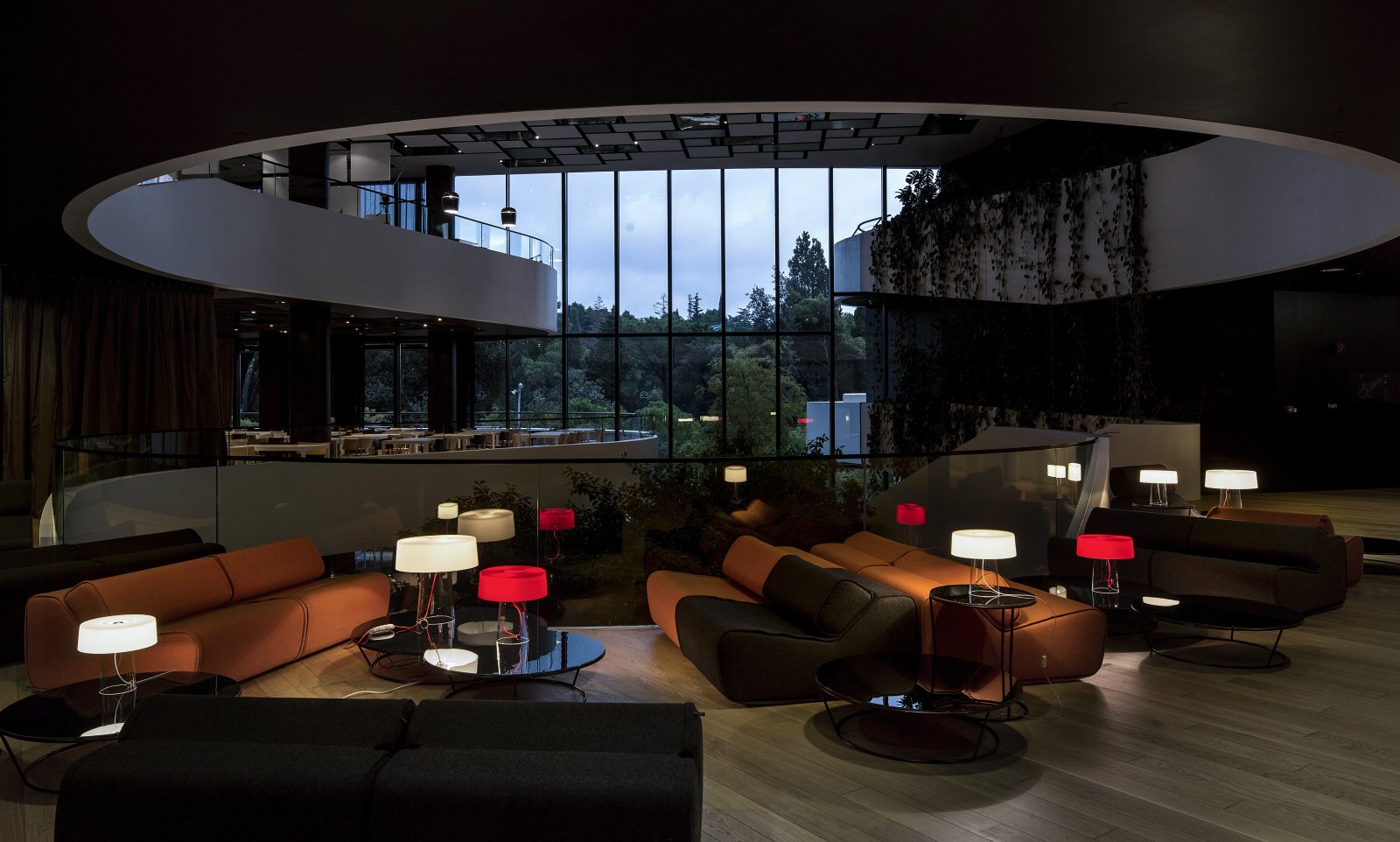 Innenaufnahme eines modernen, dunklen Loungebereichs mit bequemen Sitzsäcken und Tischlampen, großes Fenster mit Blick nach draußen, viel natürlicher Licht, elegante Architektur.