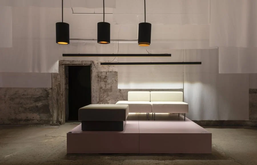 Modernes, minimalistisches Wohnzimmer mit schwarzen Hängeleuchten, weißen Möbeln und einer unvollendeten Wand im Hintergrund.