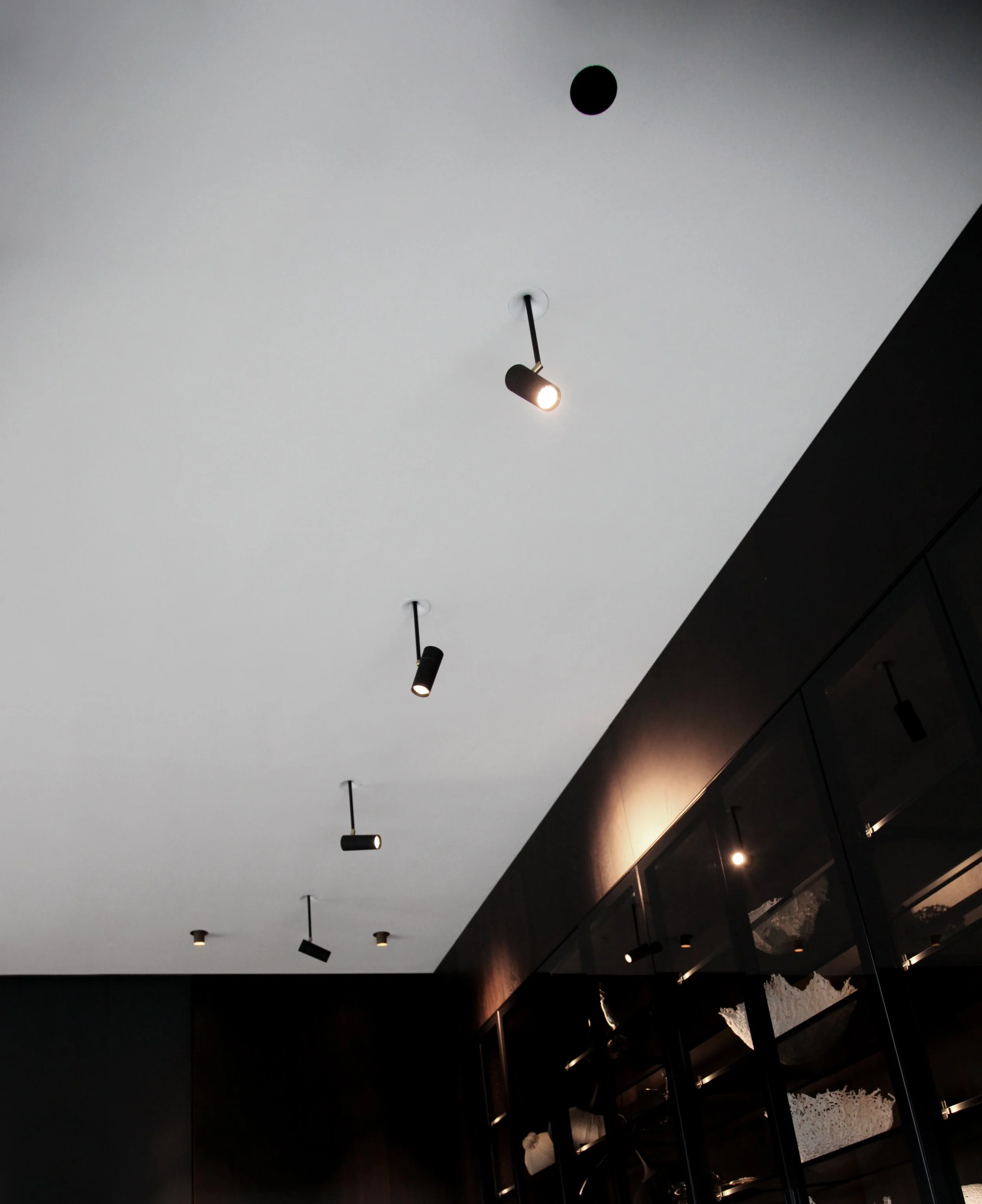 Decke mit mehreren schwarzen Spotlights und Dampfglasvitrinen seitlich.