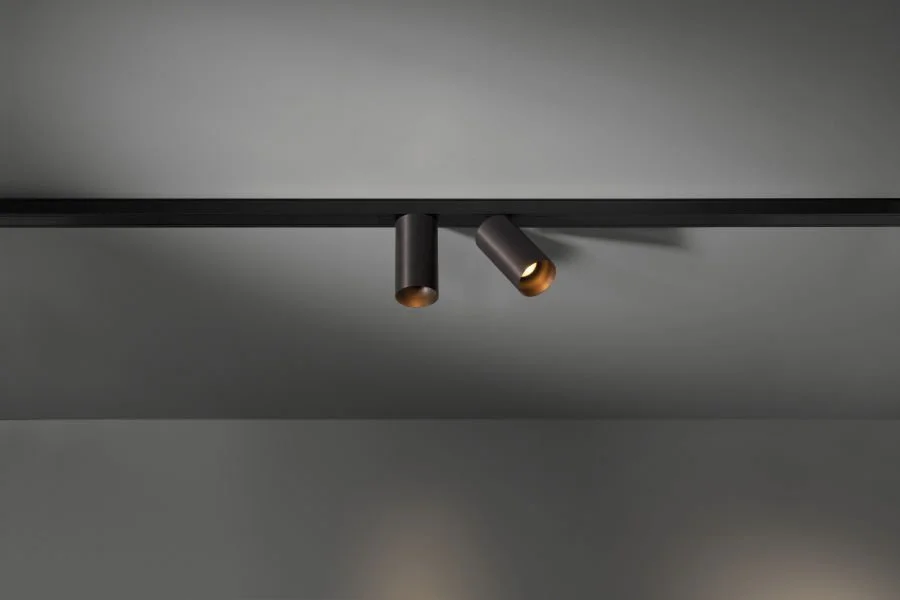 Zwei schwarze Deckenleuchten an einer Decke, eine leuchtet goldfarben im Inneren.
