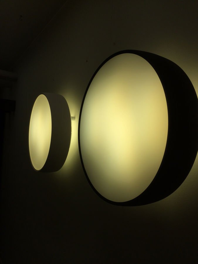 Drei beleuchtete, ovale Lichtinstallationen an einer Wand, die in warmem Gelb leuchten.